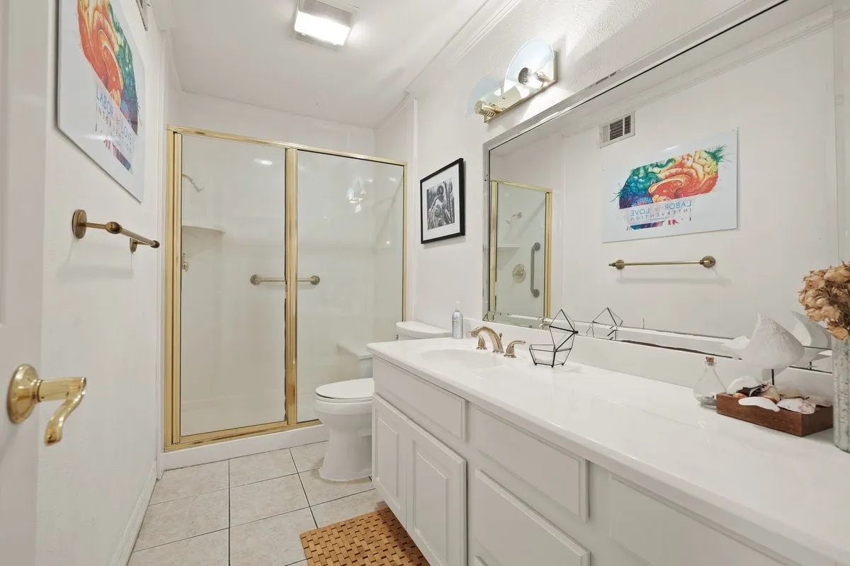 Bathroom featuring a white vanity with integrated sink, a large wall-mounted mirror, and a brass-framed glass shower enclosure