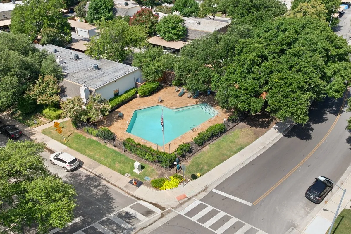 Community Pool Heart-shaped swimming pool with concrete decking, surrounded by a black metal fence and mature trees