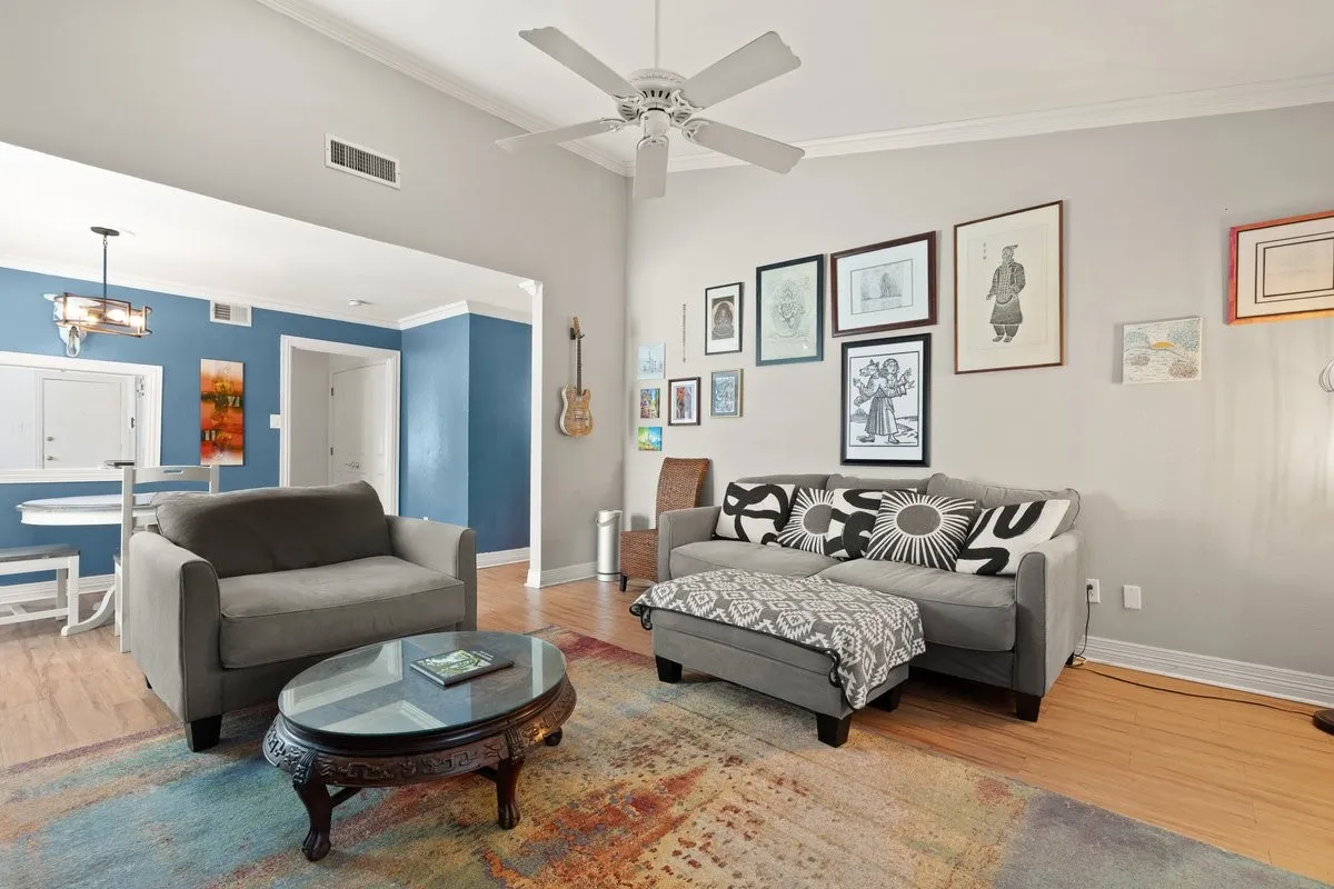 Vaulted ceiling living room featuring laminate wood-finish flooring, crown molding, and a ceiling fan