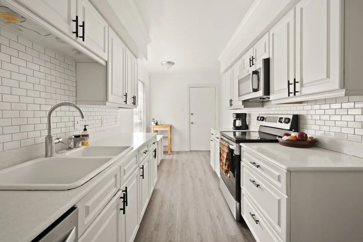 Galley kitchen featuring white cabinetry, light-colored countertops, and a subway tile backsplash