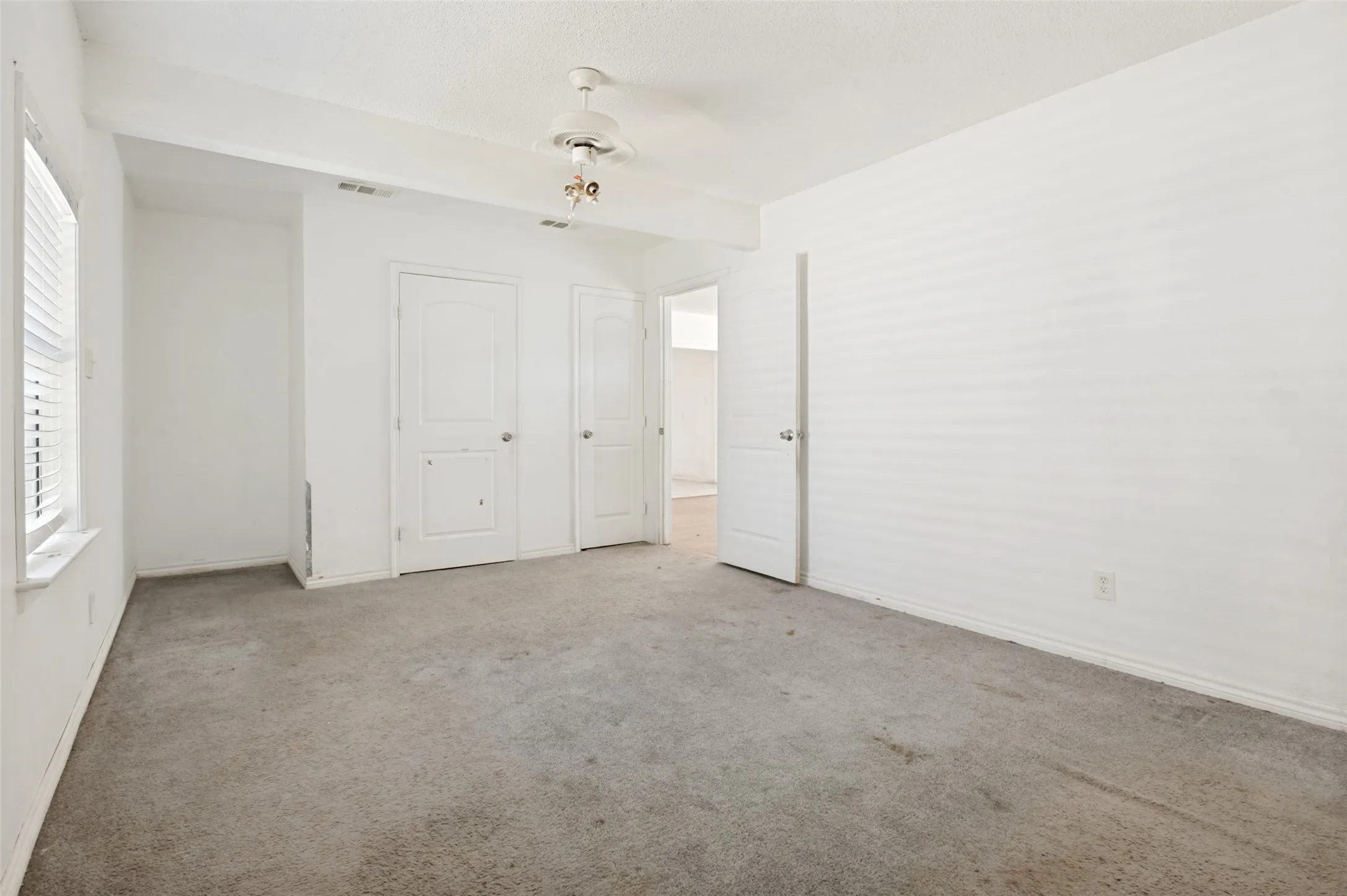 Room featuring textured carpet flooring, white walls, and a ceiling fan with integrated lighting