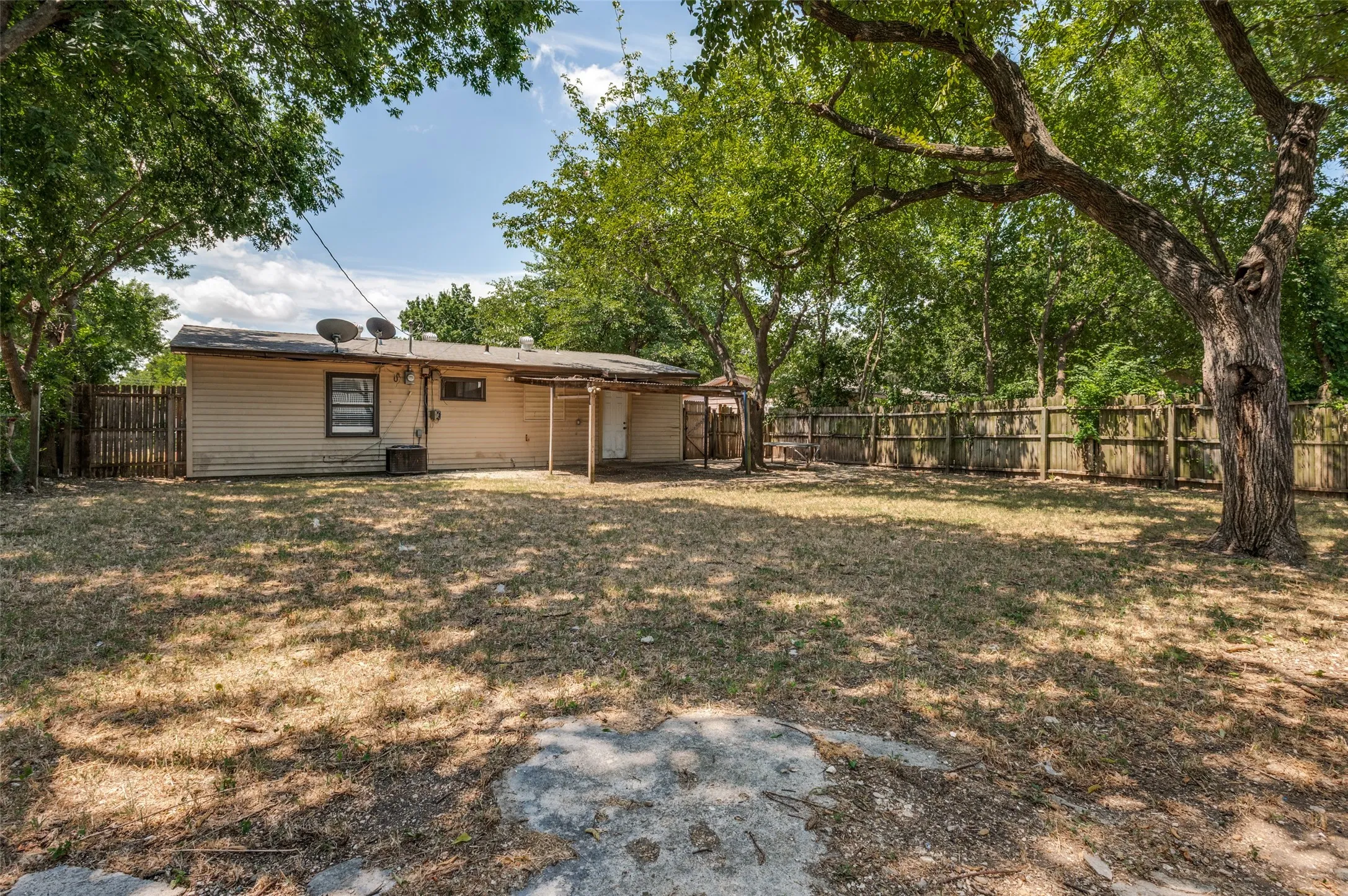 Expansive backyard featuring mature trees, a wood privacy fence, and a covered patio area