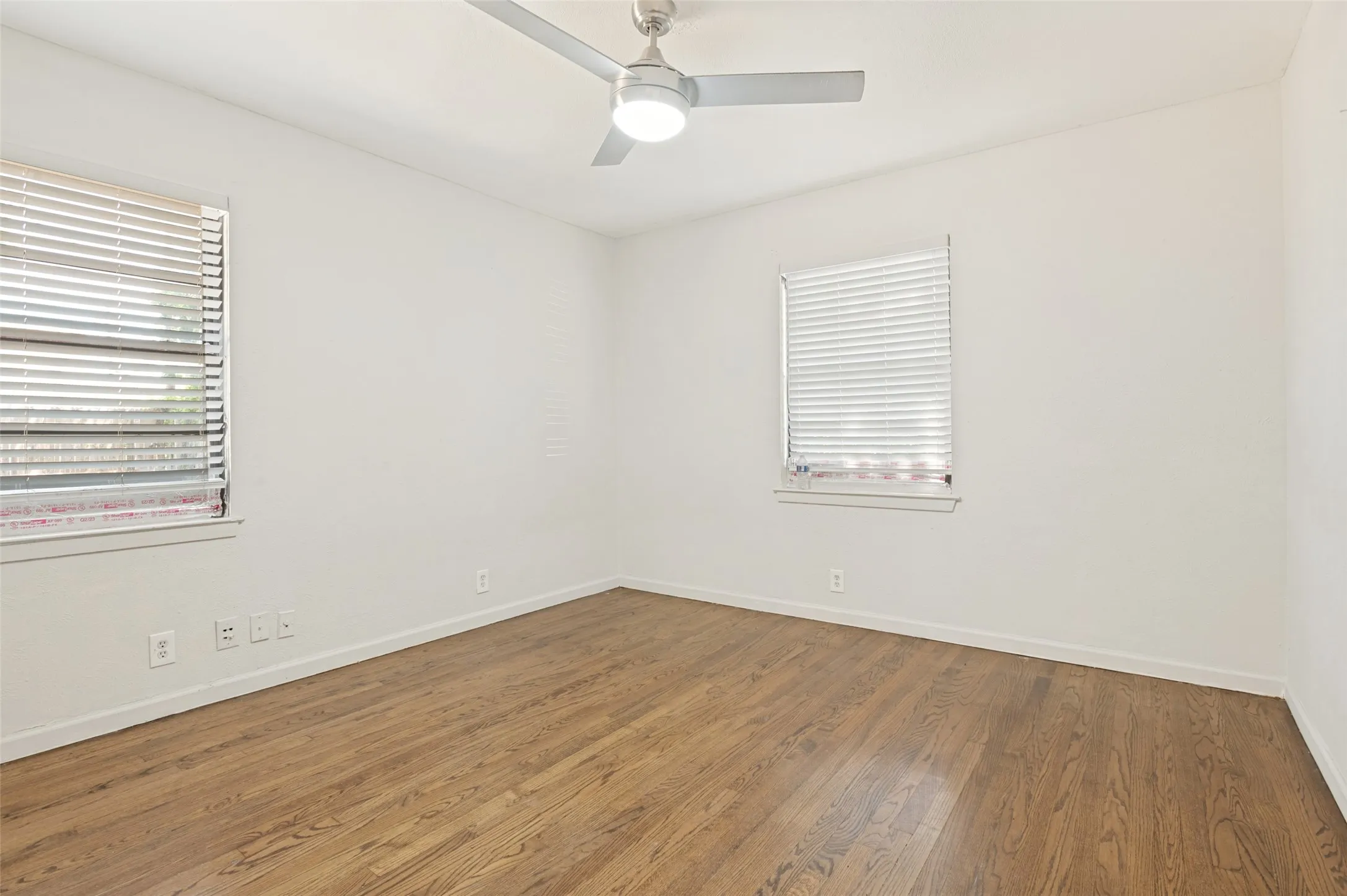 Interior room featuring wood-finish flooring, white walls, and a ceiling fan with integrated lighting
