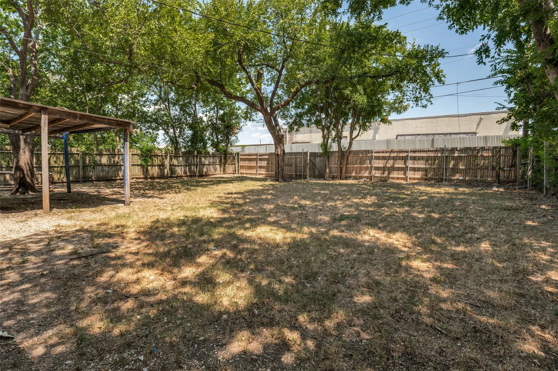 Spacious backyard featuring a wood privacy fence, mature trees, an open-air shed structure, and an expansive ground area