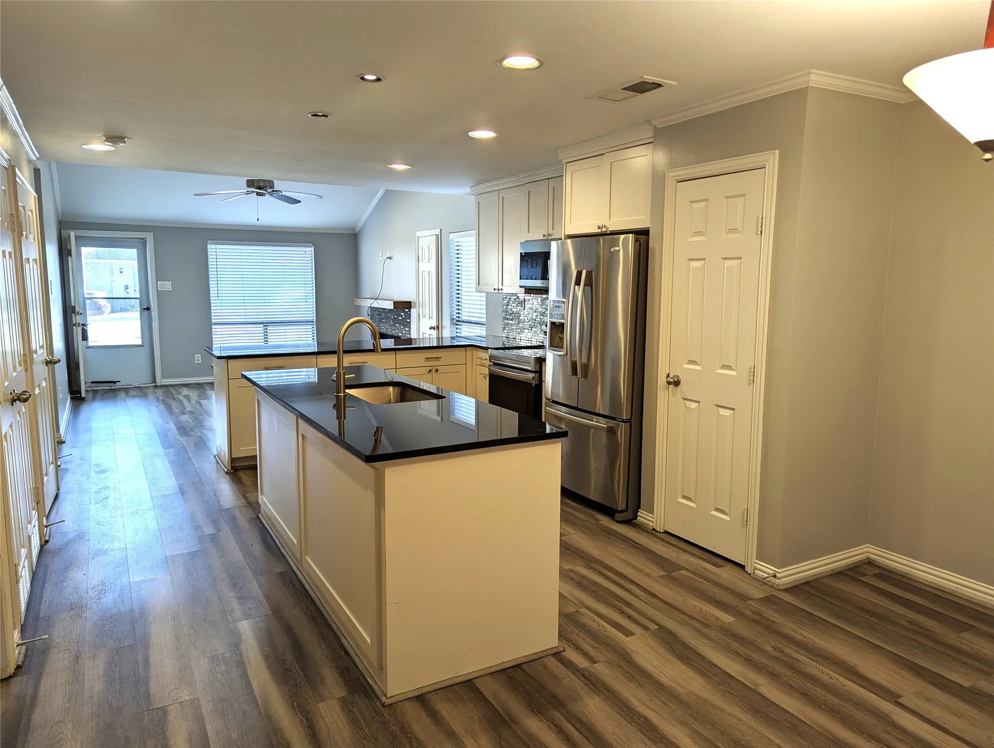 Kitchen featuring dual islands with dark countertops, white cabinetry, stainless steel appliances, and wood-finish flooring