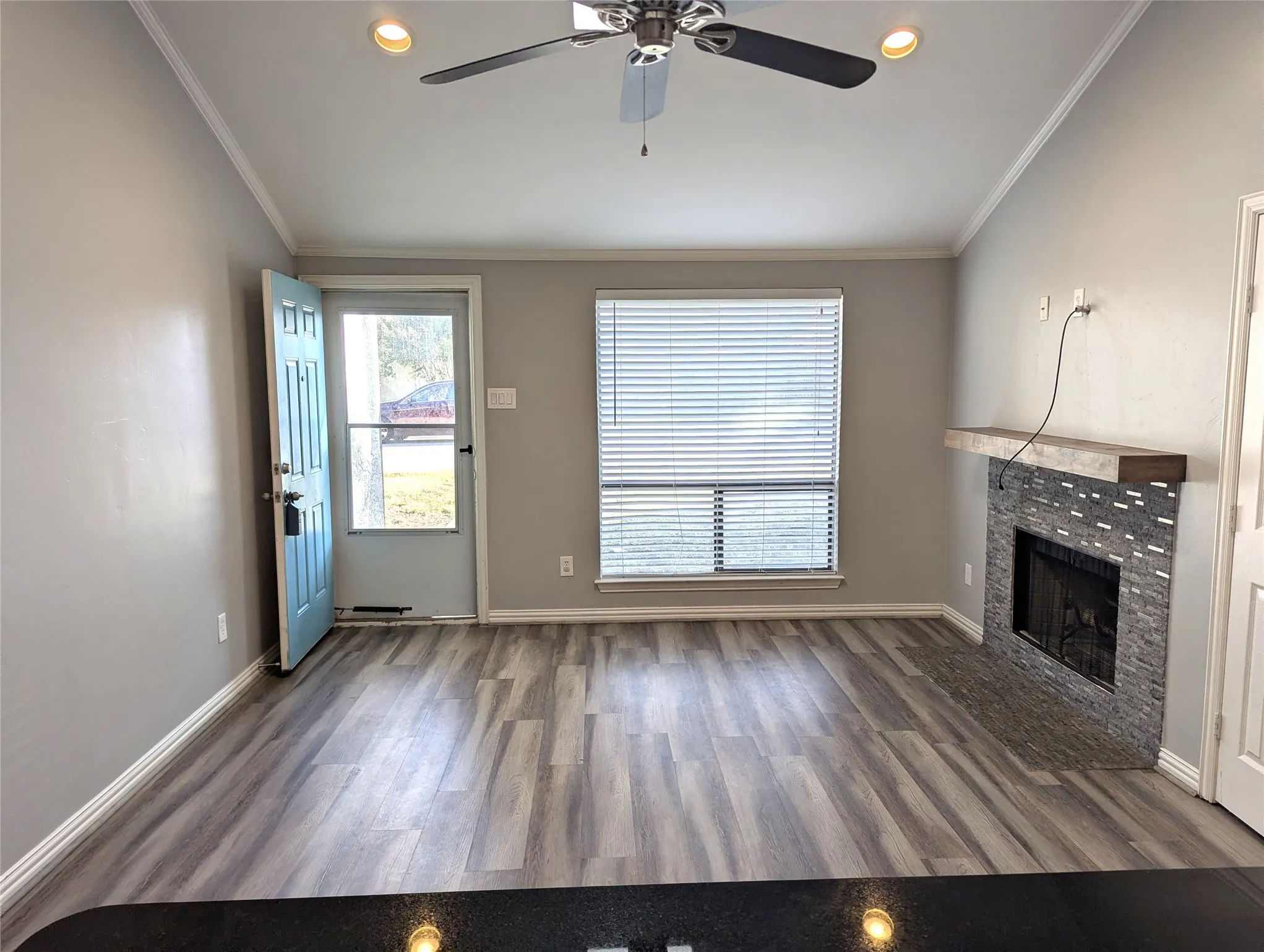 Open concept living area featuring wood-finish flooring, a fireplace with a stone surround and wood mantel, vaulted ceilings, and recessed lighting