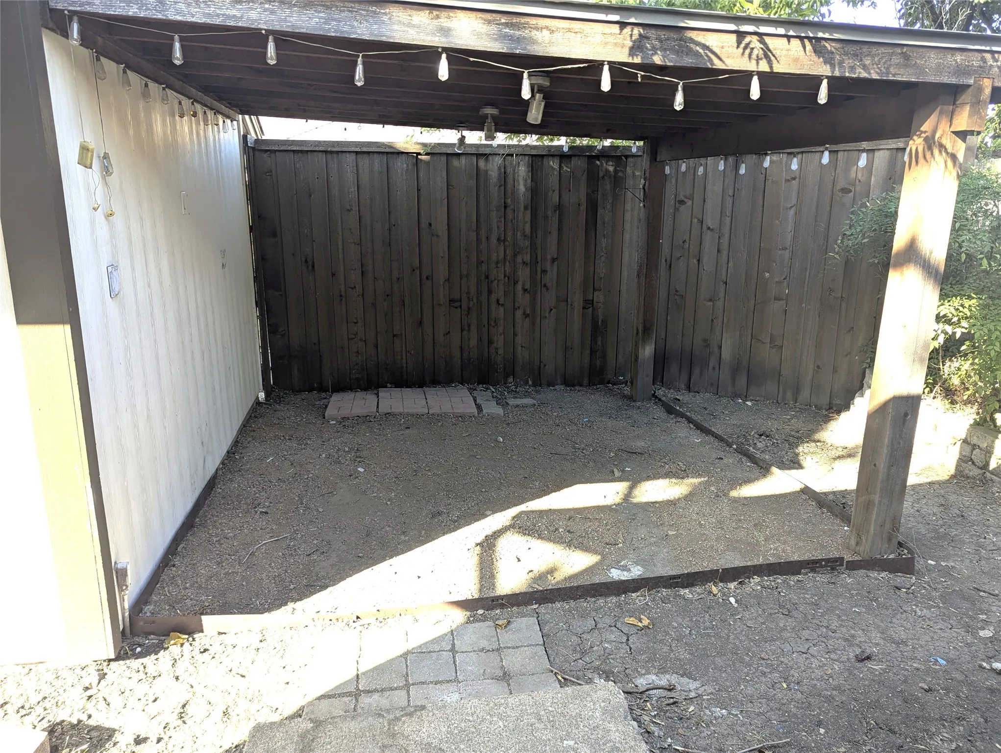 Covered outdoor area with wood beam construction, string lighting, and wood panel fencing