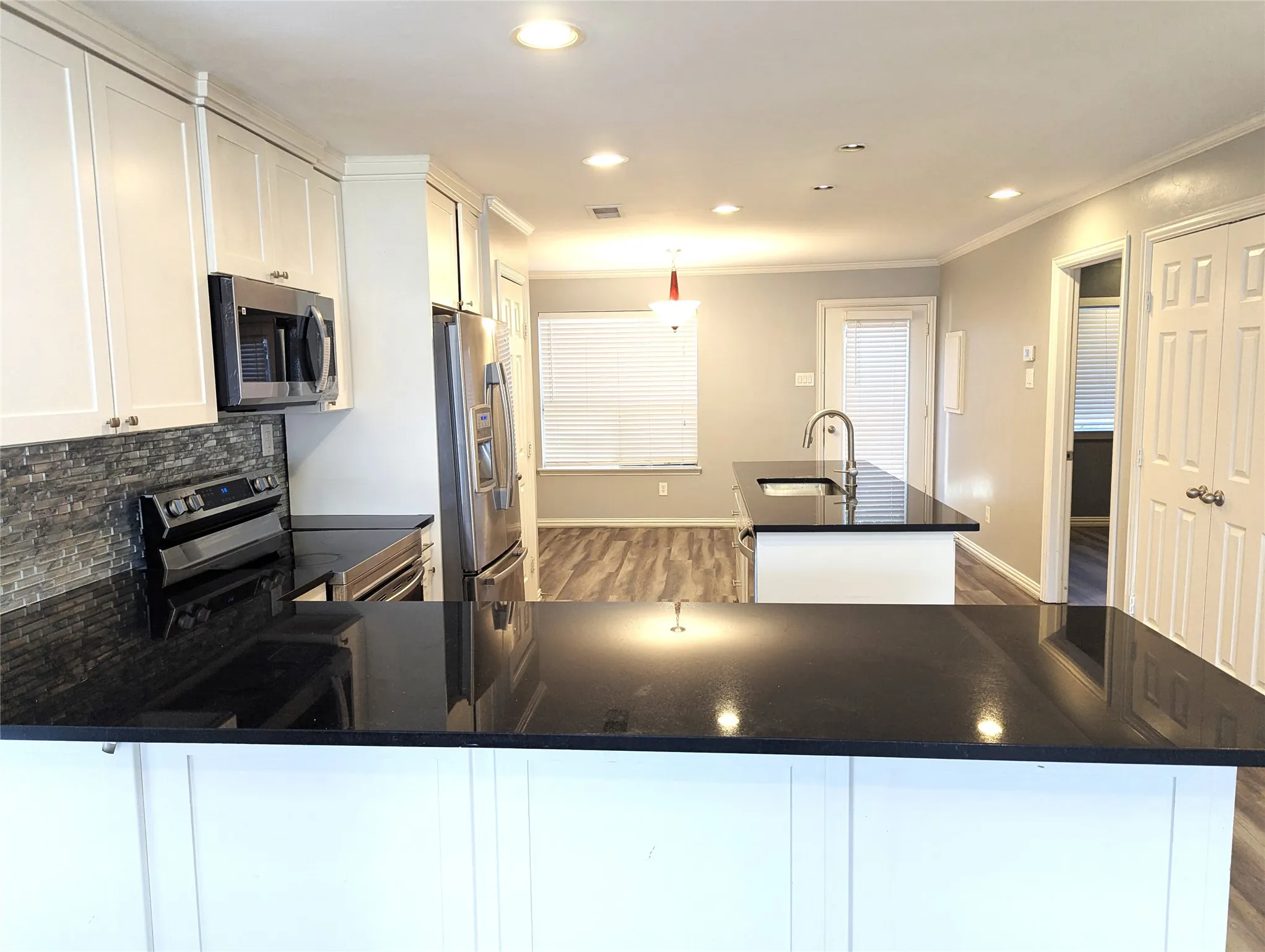 Kitchen featuring white cabinetry, stainless steel appliances, dark countertops, a stone-finish backsplash, and wood-finish flooring