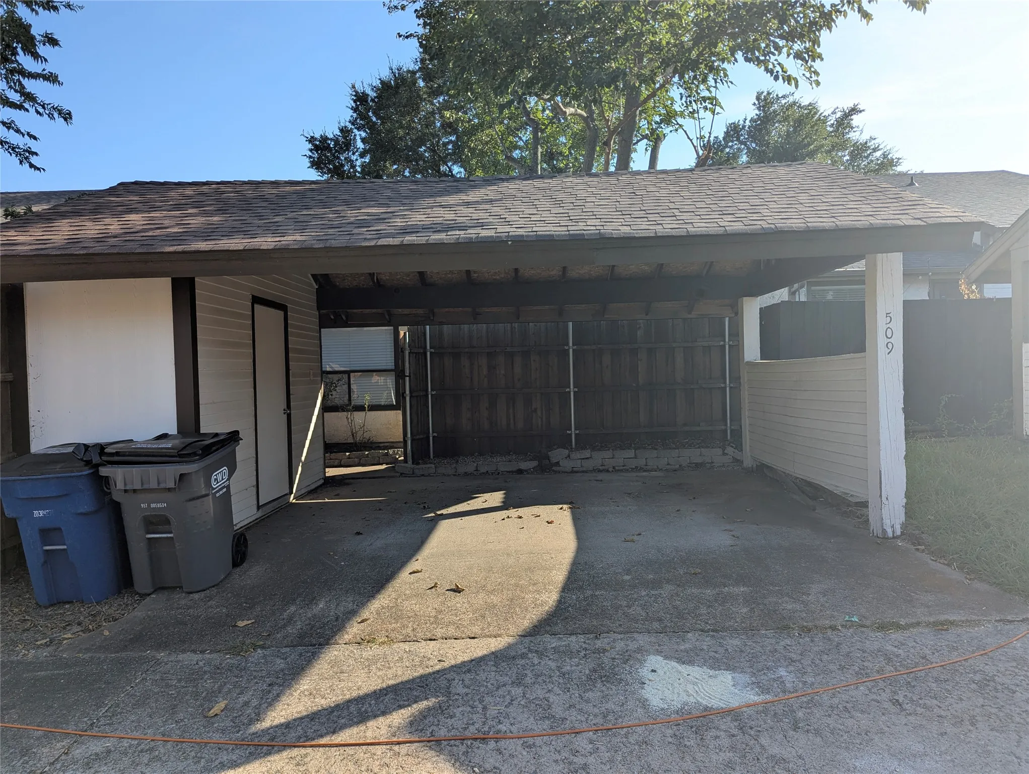 Paved carport with an attached storage shed, horizontal paneling, and a wood privacy fence