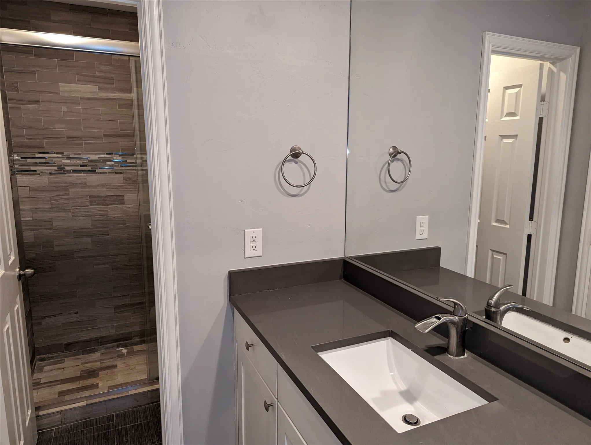 Modern bathroom vanity featuring an undermount sink, a sleek single-handle faucet, a dark countertop, white shaker-style cabinetry, and a full-width mirror