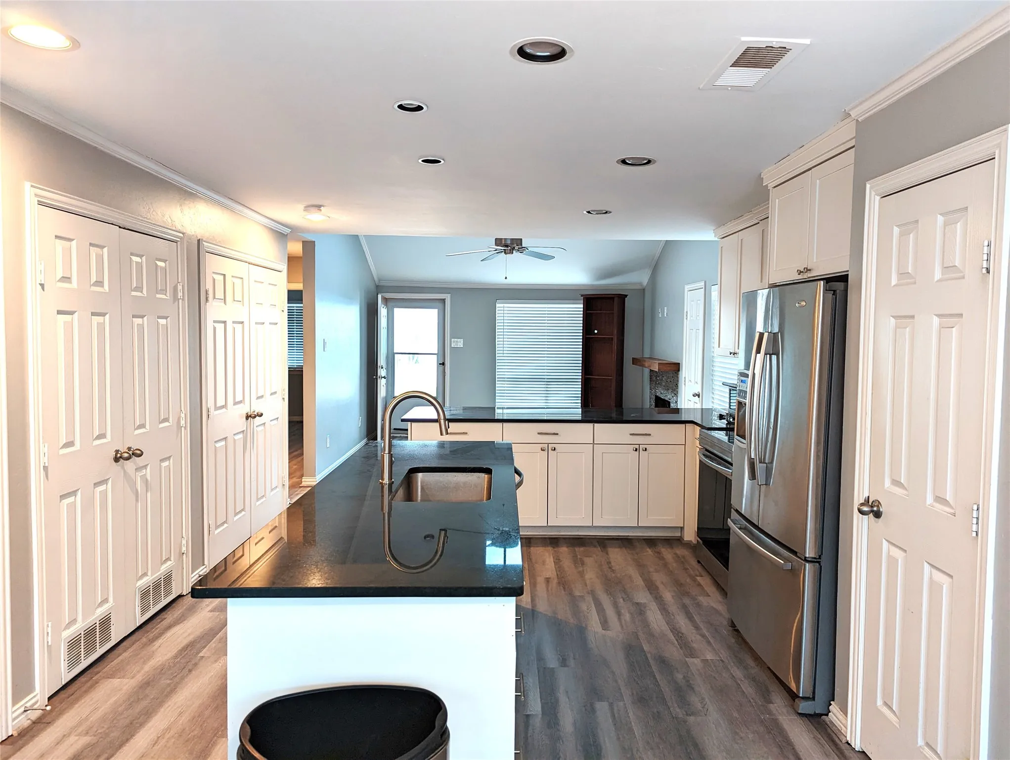 Contemporary kitchen featuring an island with an undermount sink, dark countertops, and white cabinetry