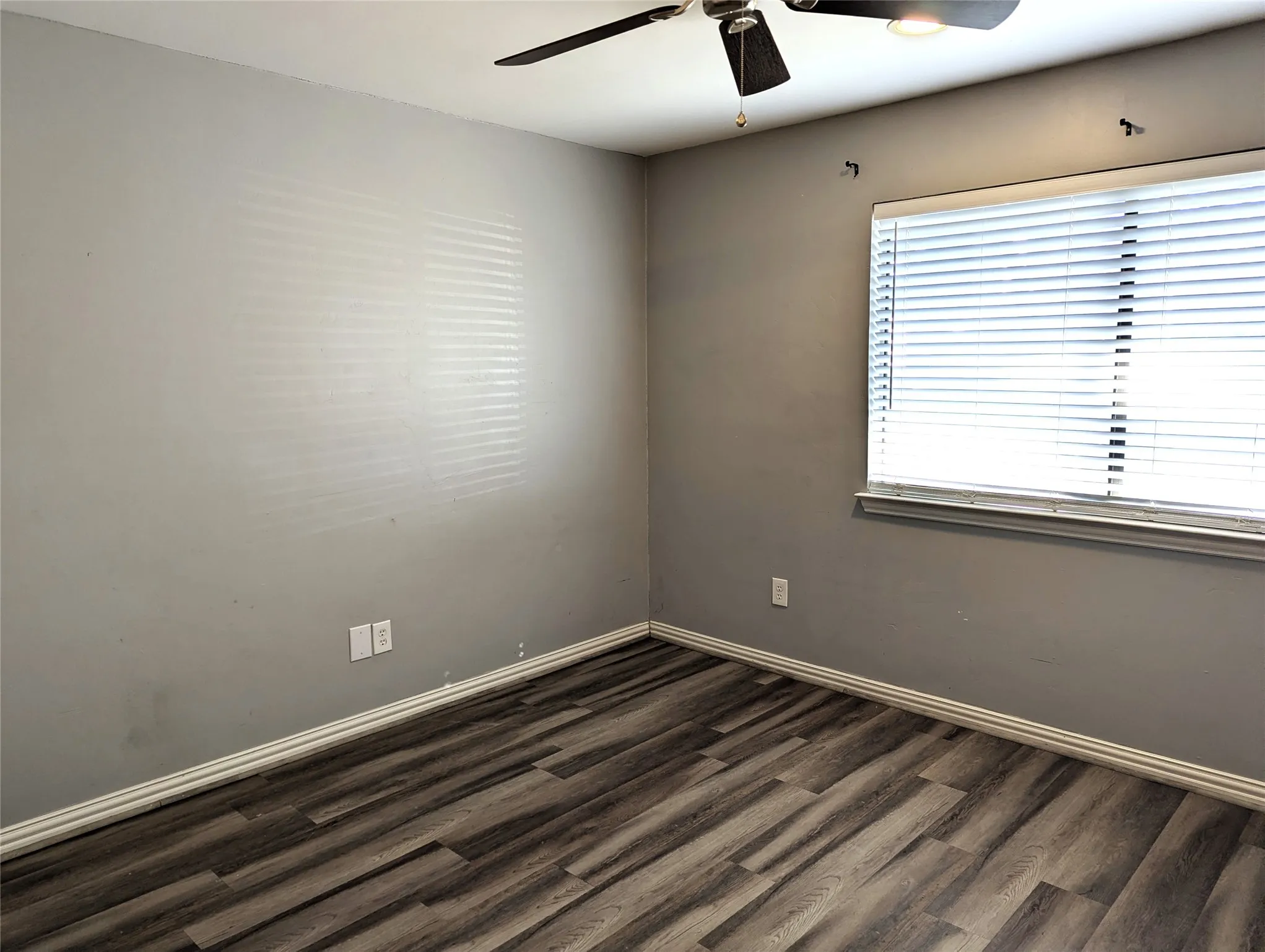 Wood-finish flooring, ceiling fan with integrated lighting, window with blinds, and light gray wall paint