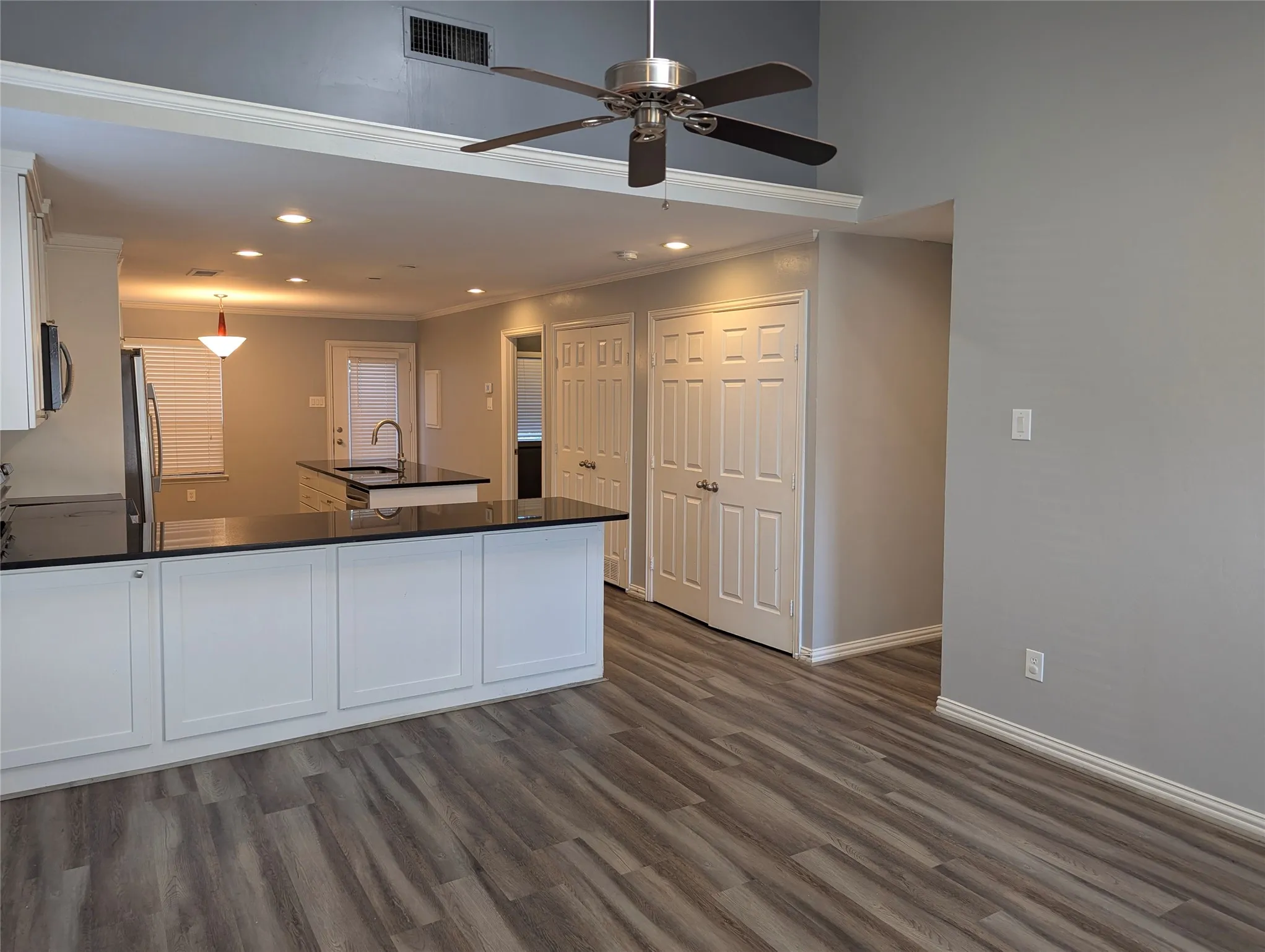 Open-concept kitchen with dark countertops, white cabinetry, a kitchen island with a sink, and wood-finish flooring