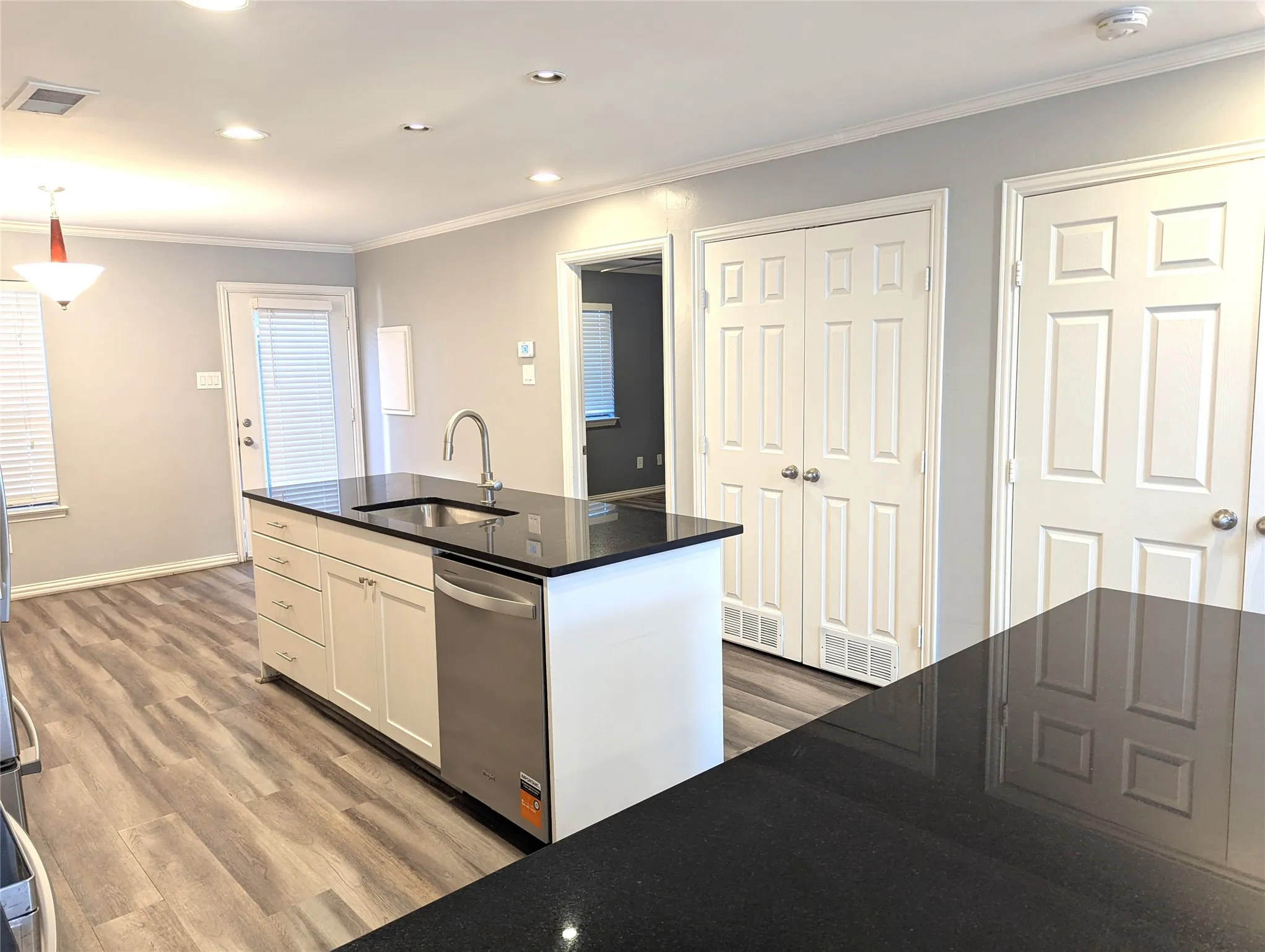 Kitchen island with dark countertops, wood-finish flooring, white cabinetry, stainless steel sink, and recessed lighting