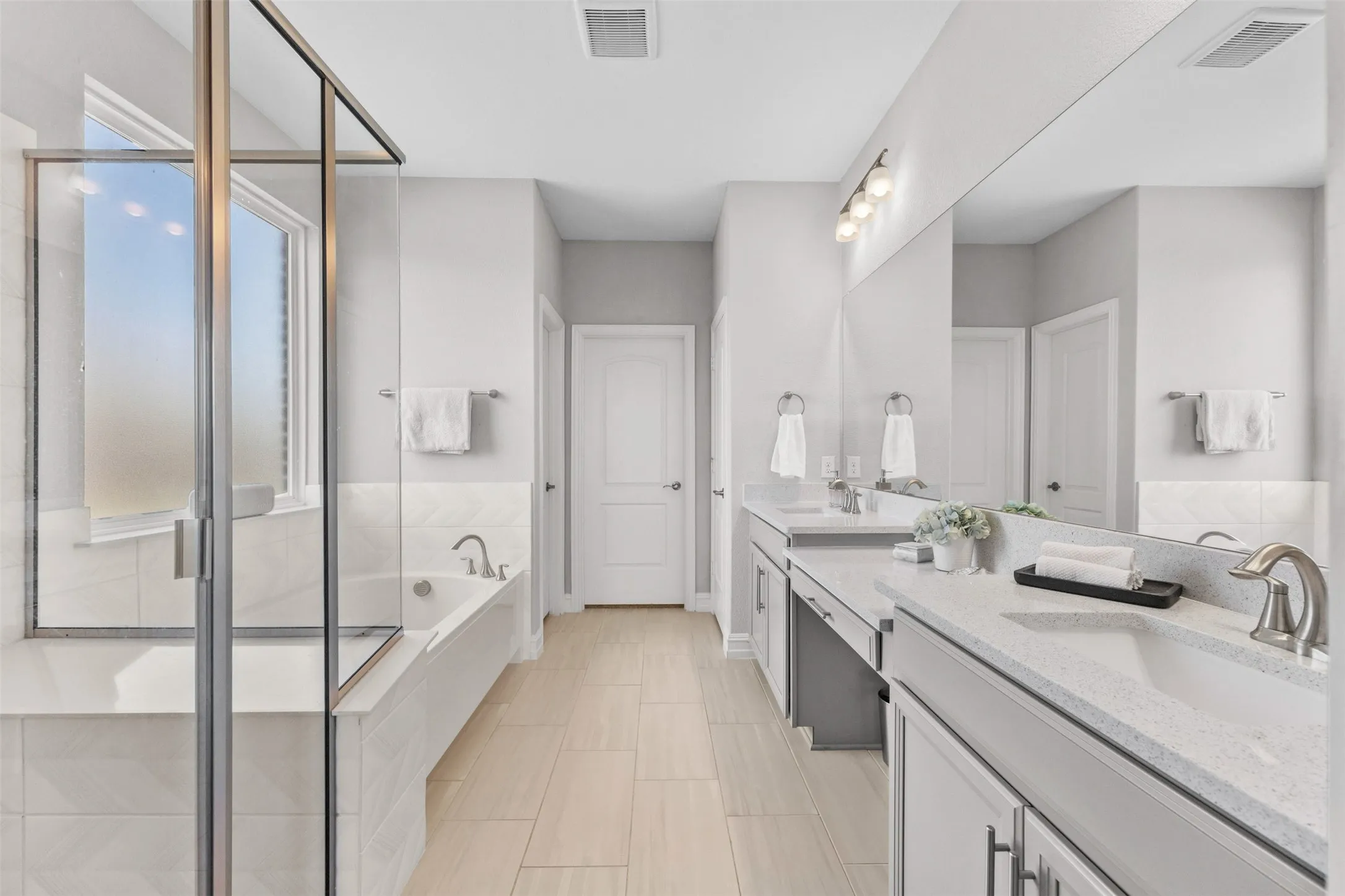Bathroom featuring a glass-enclosed shower, a built-in bathtub with tiled surround, and dual vanity sinks with light-toned countertops and under-sink cabinetry