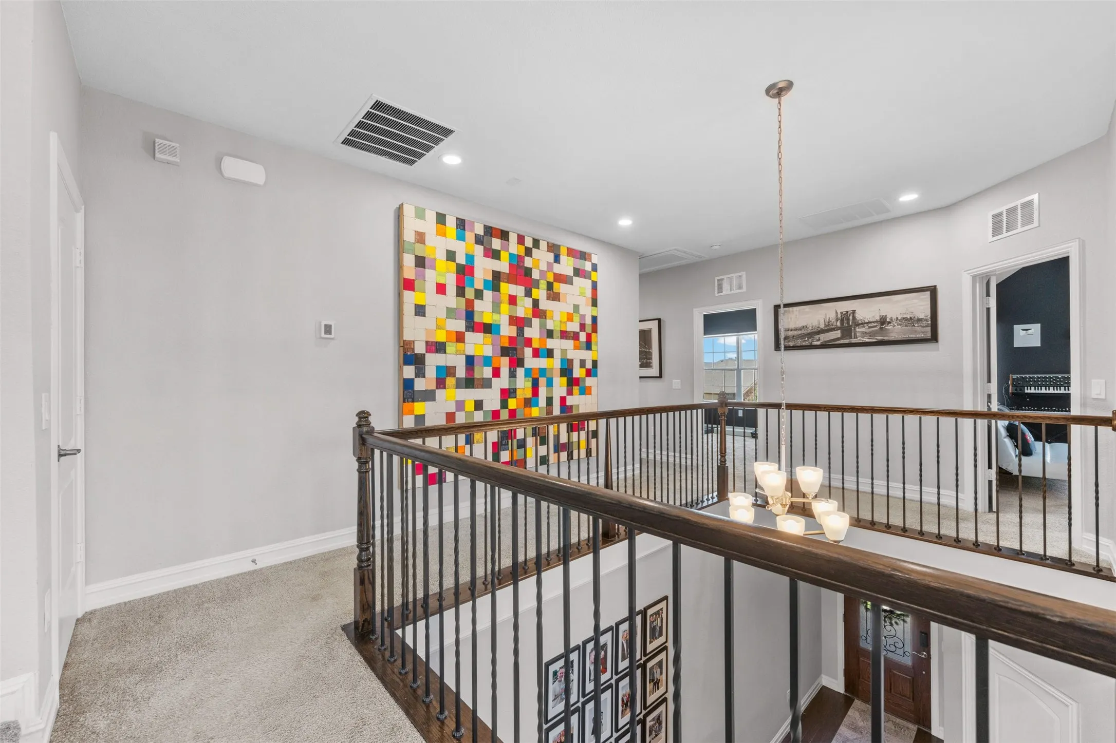 Upper-level hallway featuring a dark wood handrail with decorative metal balusters and overhead chandelier lighting