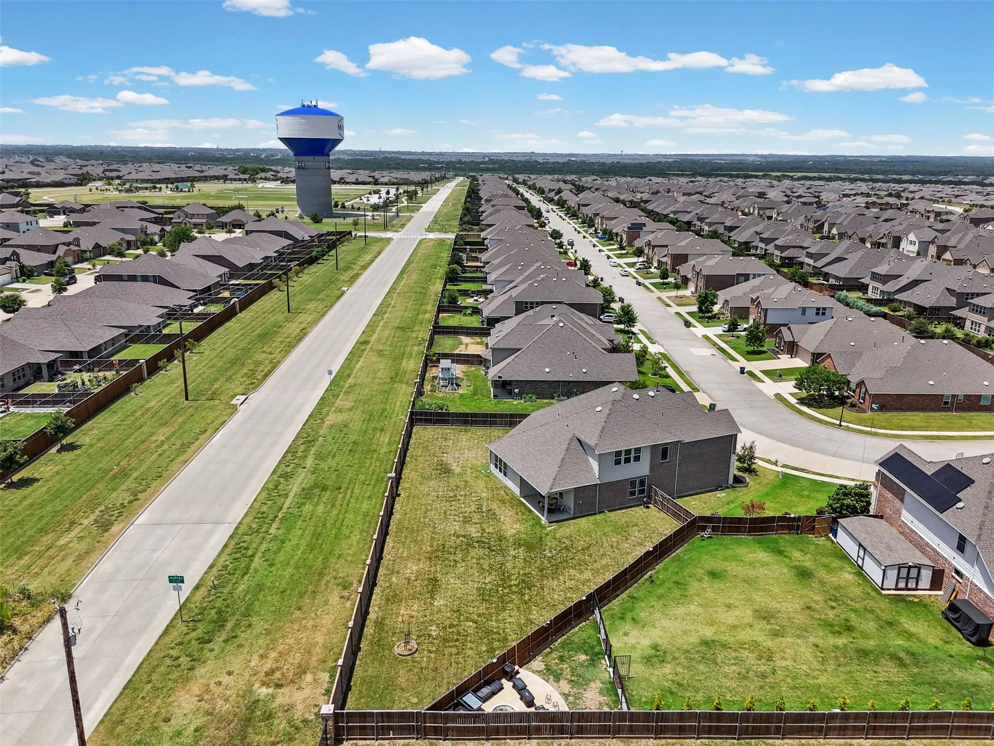 Aerial property view featuring a spacious backyard with a private fence, an outdoor fire pit area, and a detached storage shed