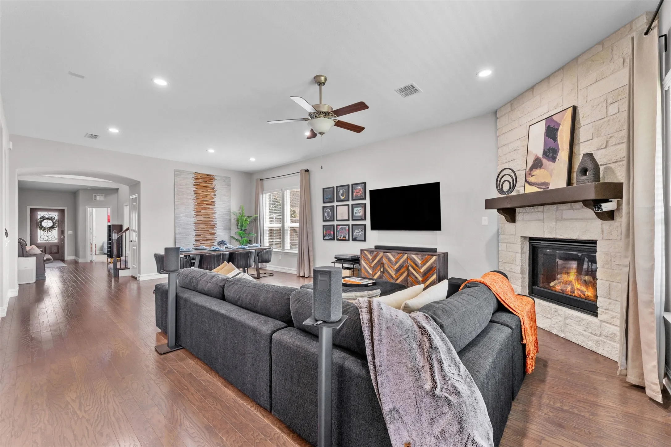 Spacious living area featuring wood-finish flooring, a stone-clad fireplace with a wood mantel, and recessed lighting