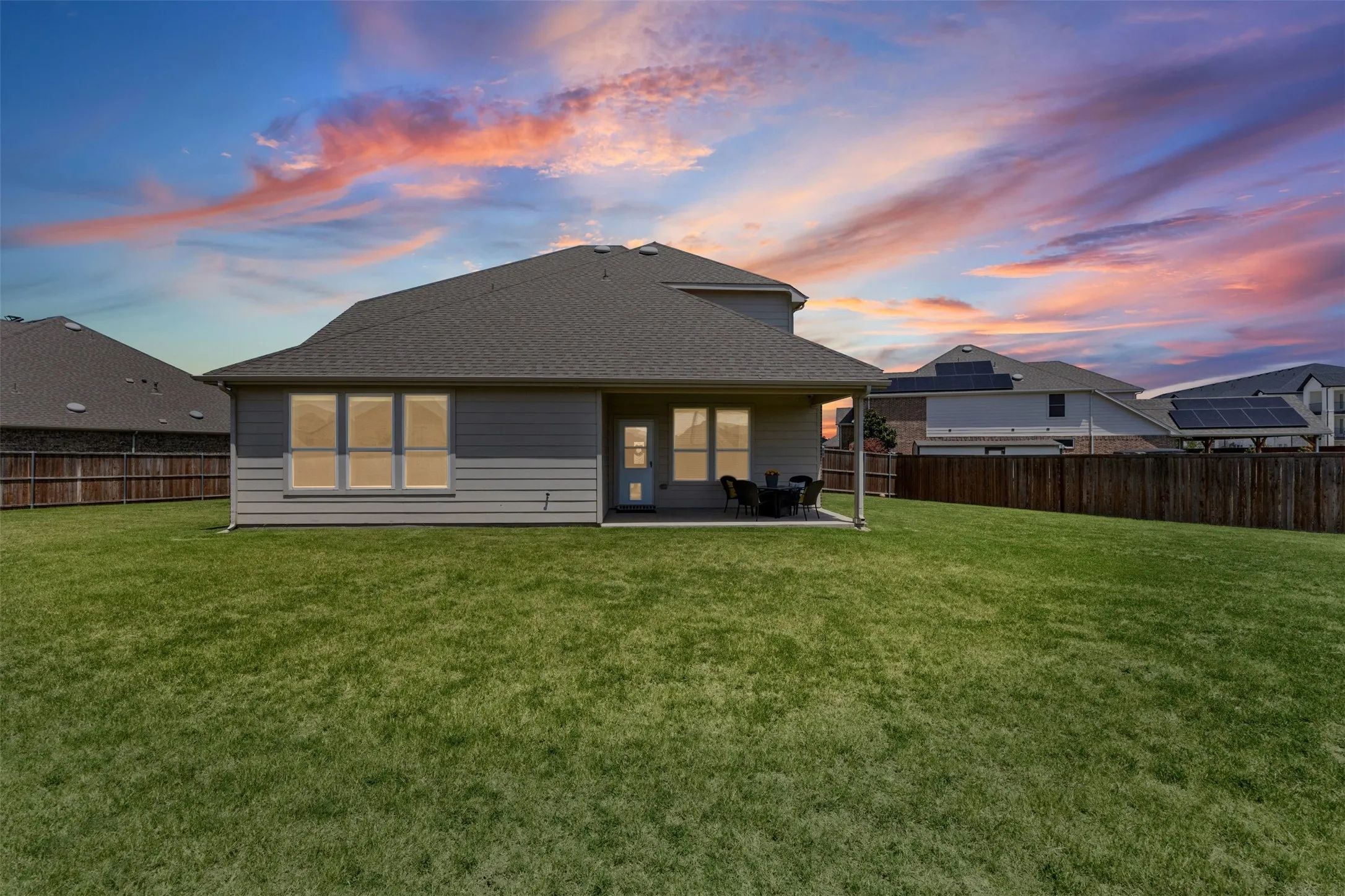 Expansive green lawn with a covered patio, privacy fencing, and a multi-pane window configuration