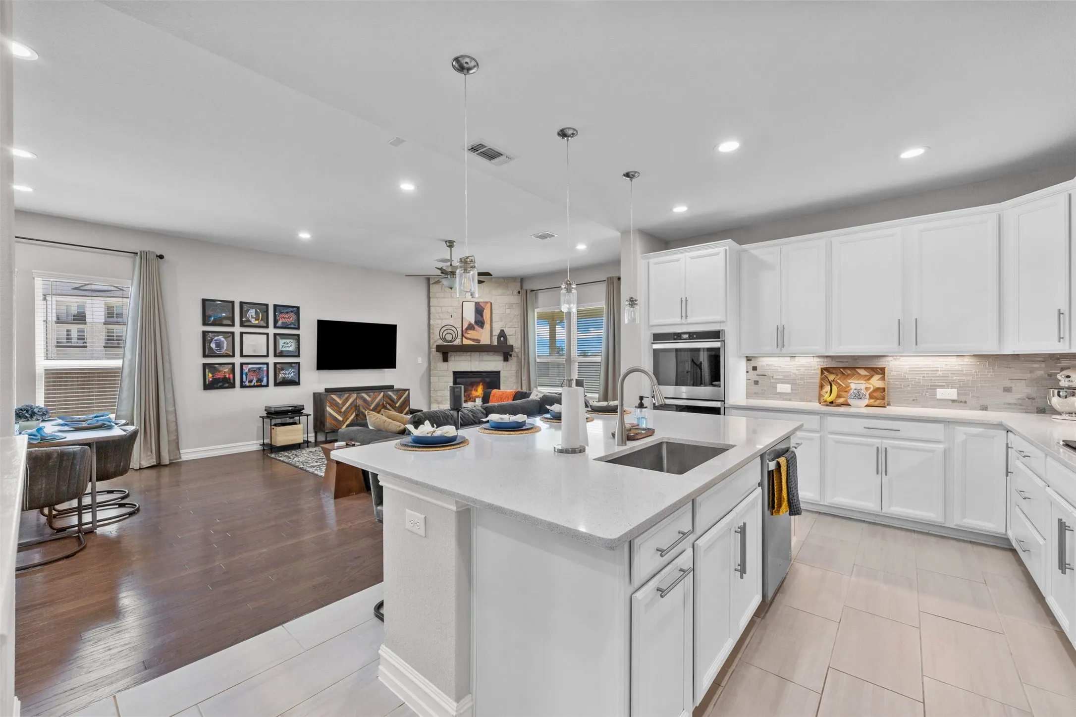 Modern kitchen featuring a large island with sink, white shaker cabinetry, stainless steel appliances, and light tile flooring