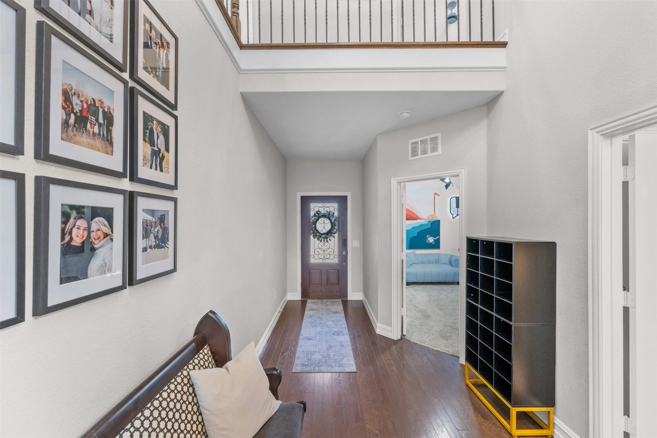 Two-story entryway featuring dark wood-finish flooring, a decorative front door with an ornate glass panel, and a second-story landing with white balusters