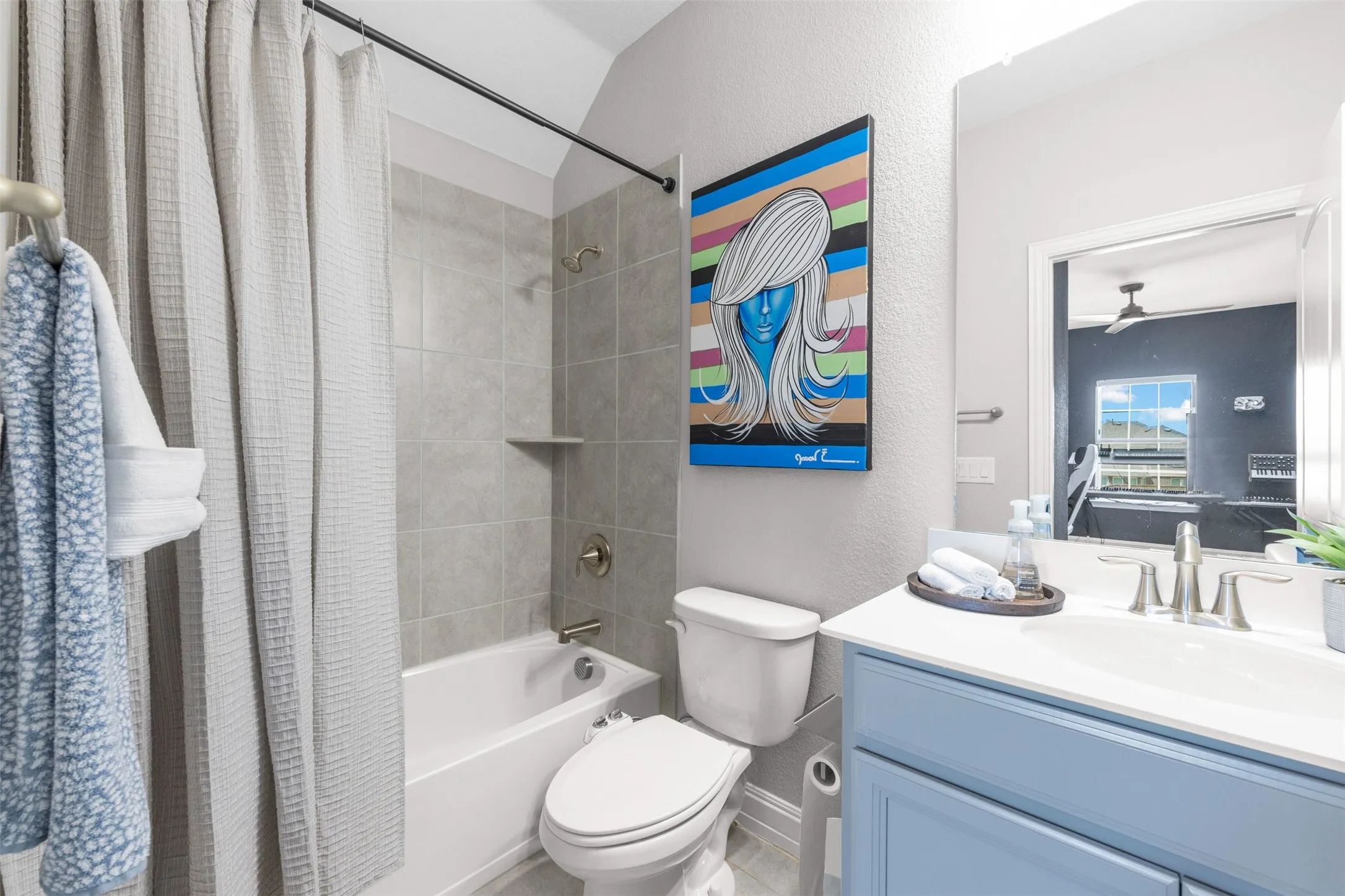 Bathroom featuring a white bathtub, gray tiled shower surround with built-in shelf, brushed nickel fixtures, and a light blue vanity with a white countertop and integrated sink