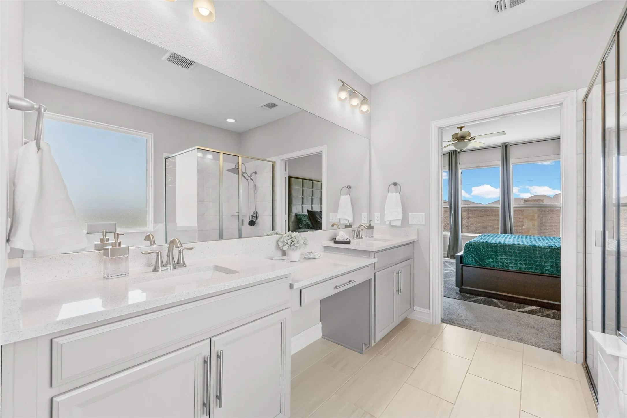 Contemporary bathroom featuring a double vanity with quartz countertops, a dedicated vanity seating area, a large walk-in shower with glass enclosure, and light tile flooring