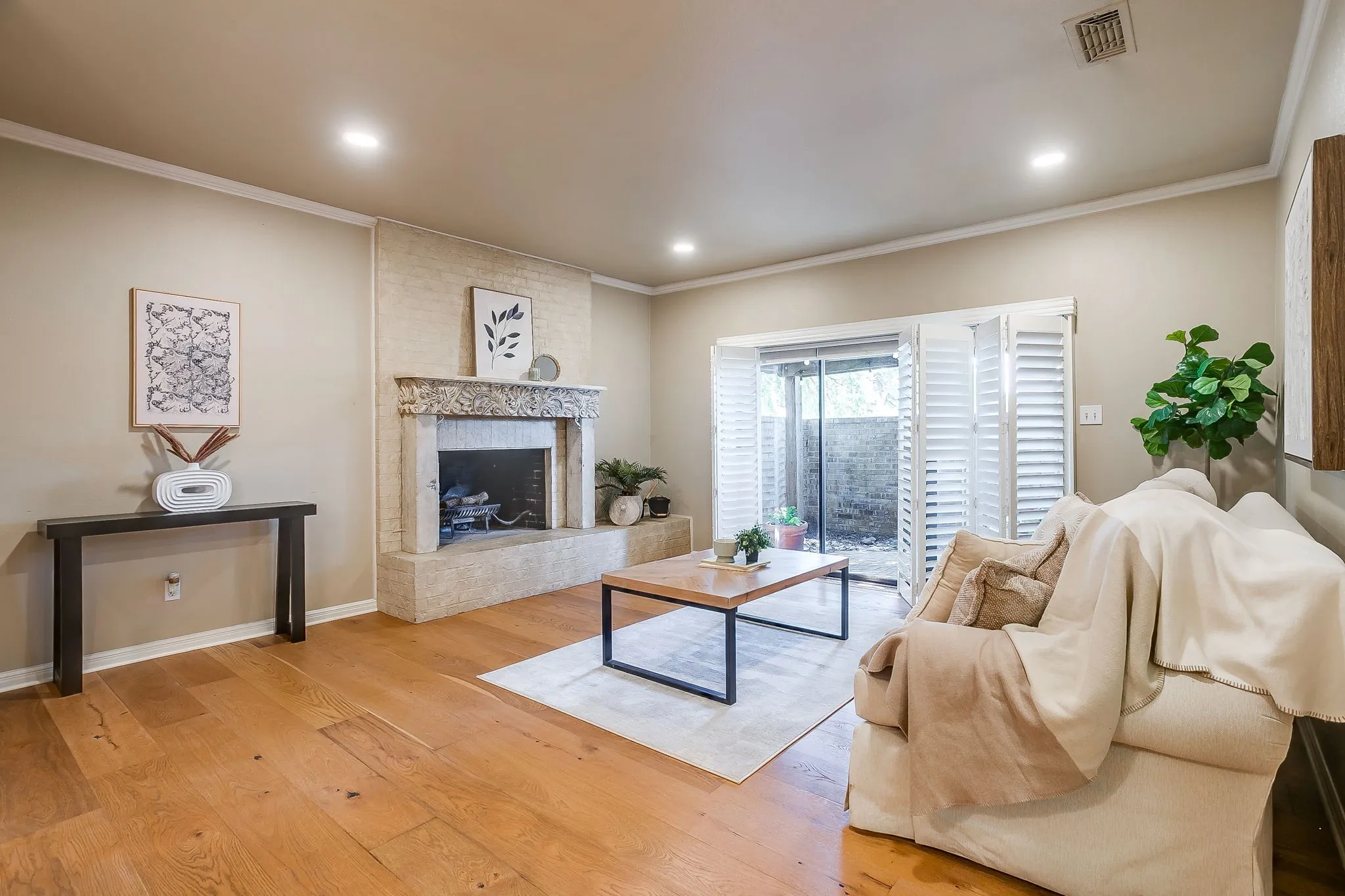 Living area featuring a textured stone fireplace with an ornate mantel, wide-plank wood-finish flooring, recessed lighting, crown molding, and French doors with plantation shutters