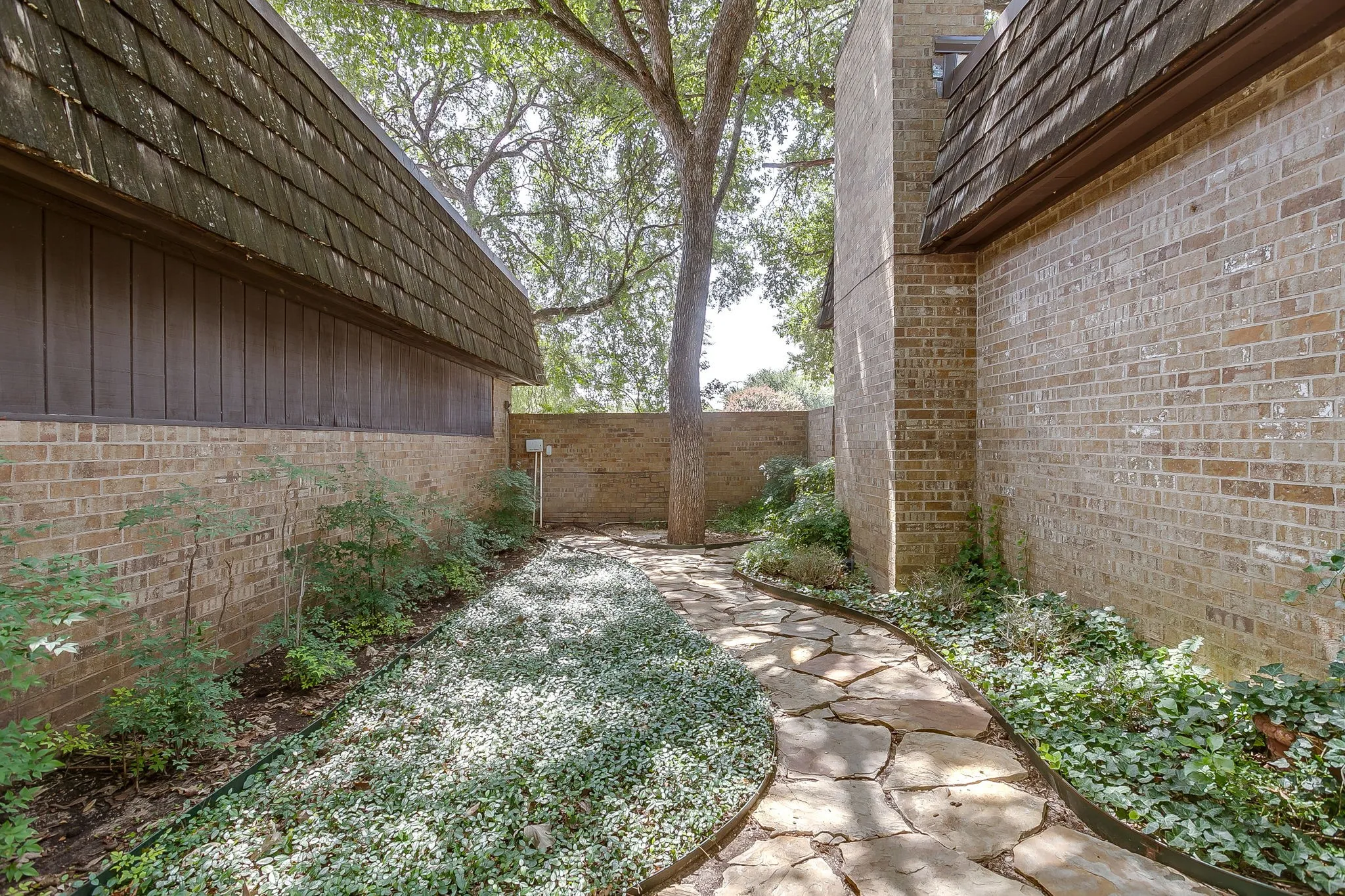 Stone pathway through landscaped grounds, bordered by brick and siding structures with textured rooflines