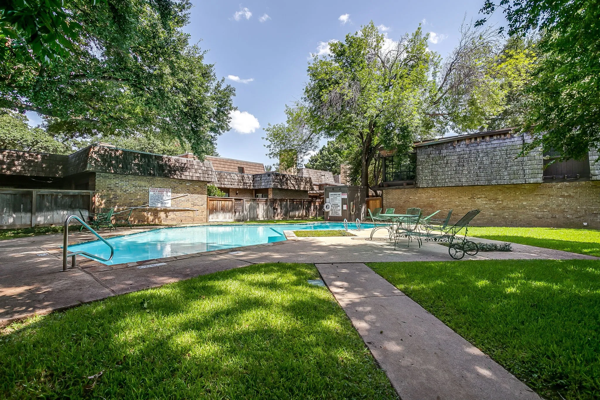 Outdoor swimming pool with concrete decking, surrounded by a lawn area and mature trees
