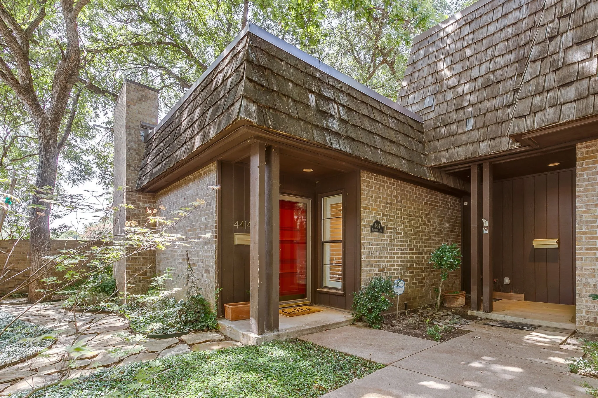 Brick exterior featuring a bright red entry door, natural wood shake roof, and a flagstone pathway