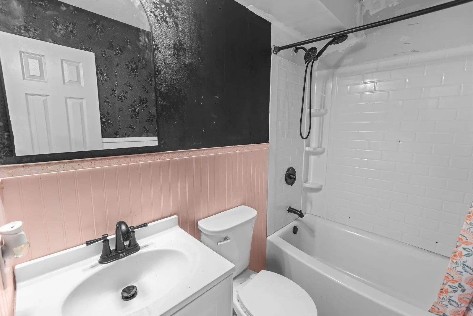 Bathroom featuring a white vanity with integrated sink, black faucet, white toilet, pink wainscoting, and a white subway tile pattern shower surround with black fixtures