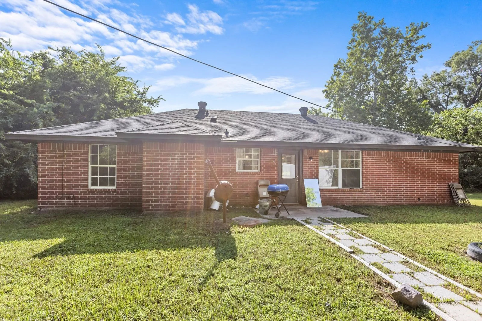 Brick exterior residence featuring a dark shingle roof and a concrete patio