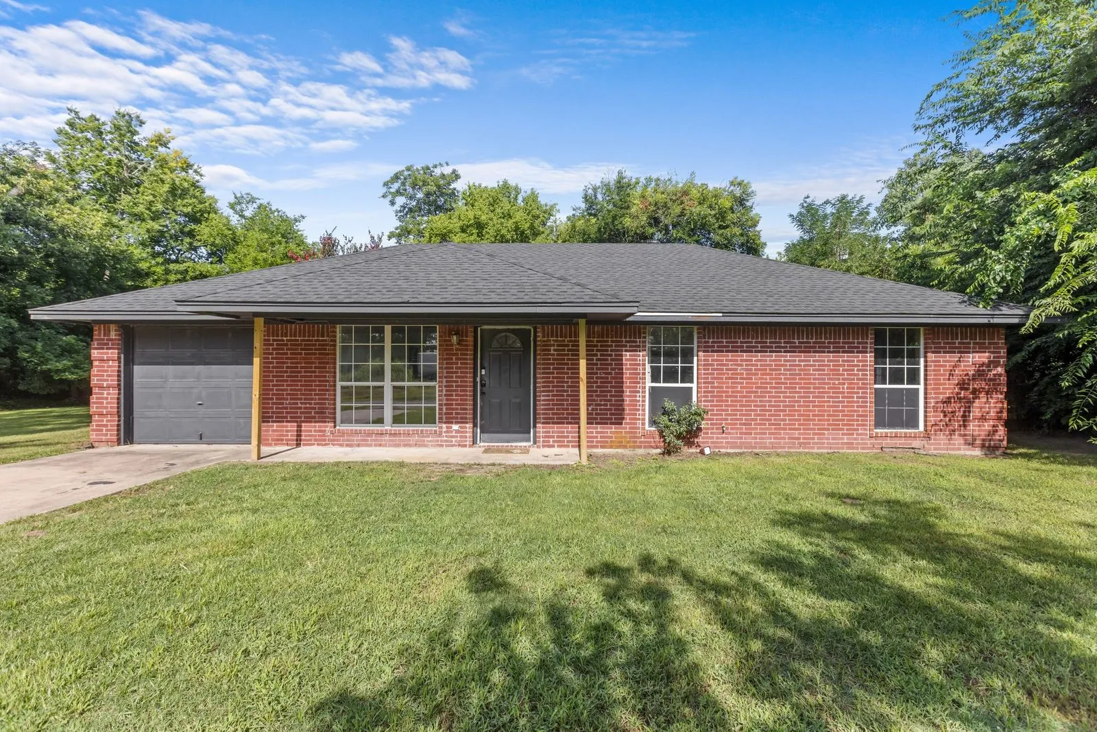 Red brick exterior featuring a dark gray roof, an attached garage with a dark gray door, and multiple windows