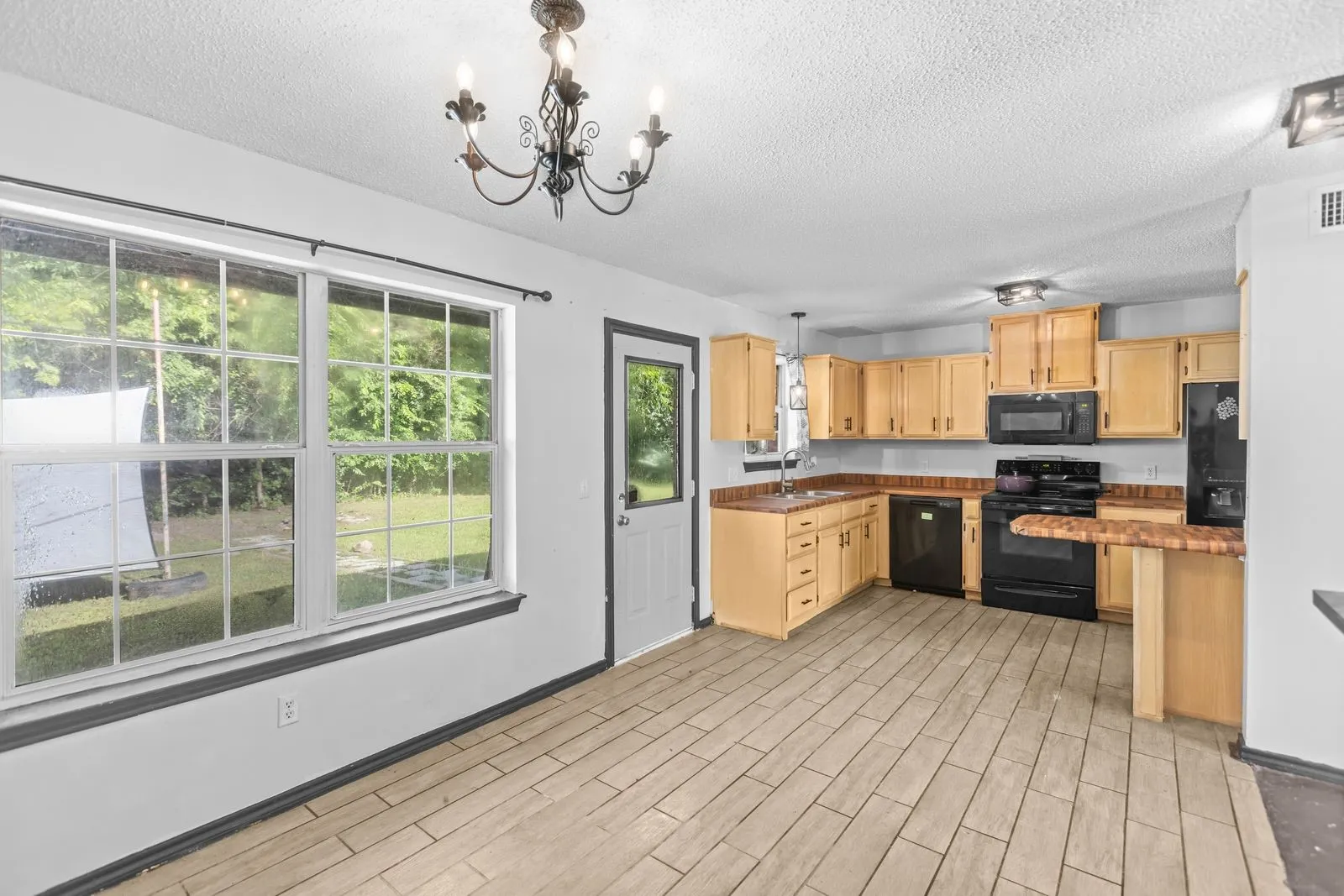 Open-concept kitchen and dining area featuring wood-finish tile flooring, natural wood cabinetry, black appliances, and a breakfast bar