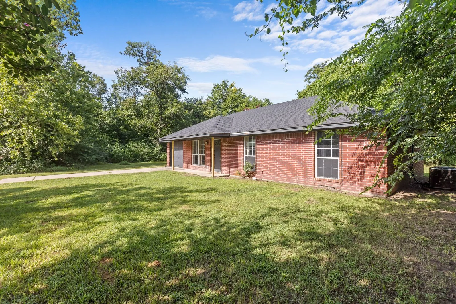Brick exterior home featuring a dark shingle roof, white-framed windows, and a covered entry with columns