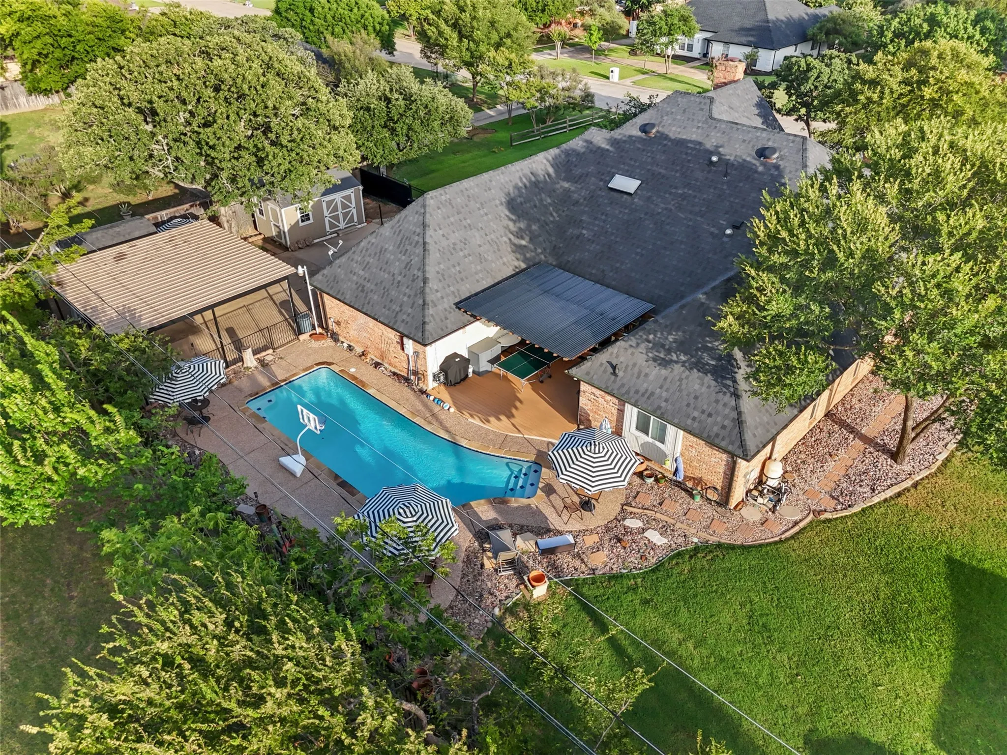 Expansive backyard featuring a free-form swimming pool, covered patio, wood-finish deck, and mature landscaping