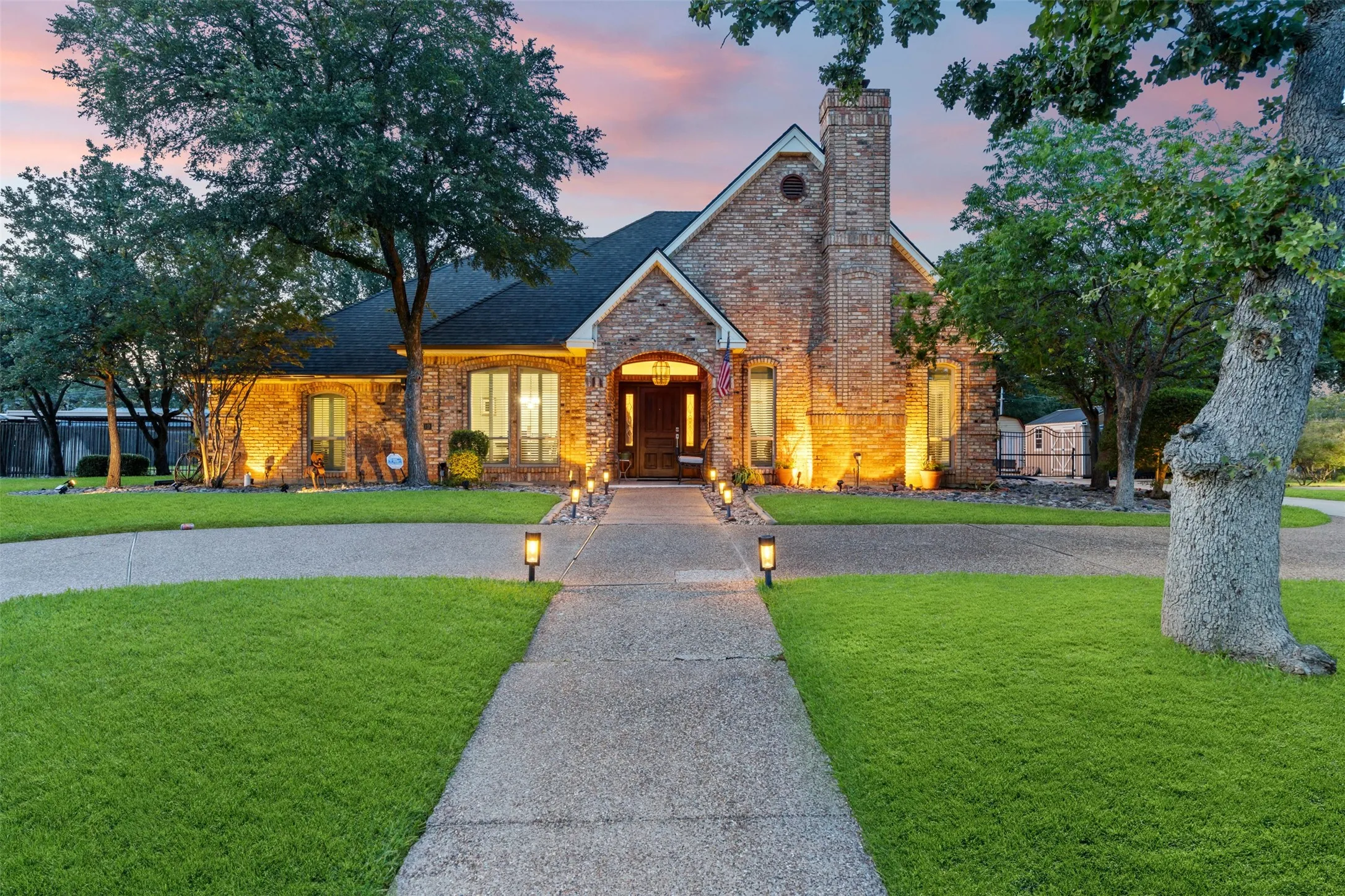 Brick exterior residence with a prominent chimney, dark shingle roof, and a concrete pathway