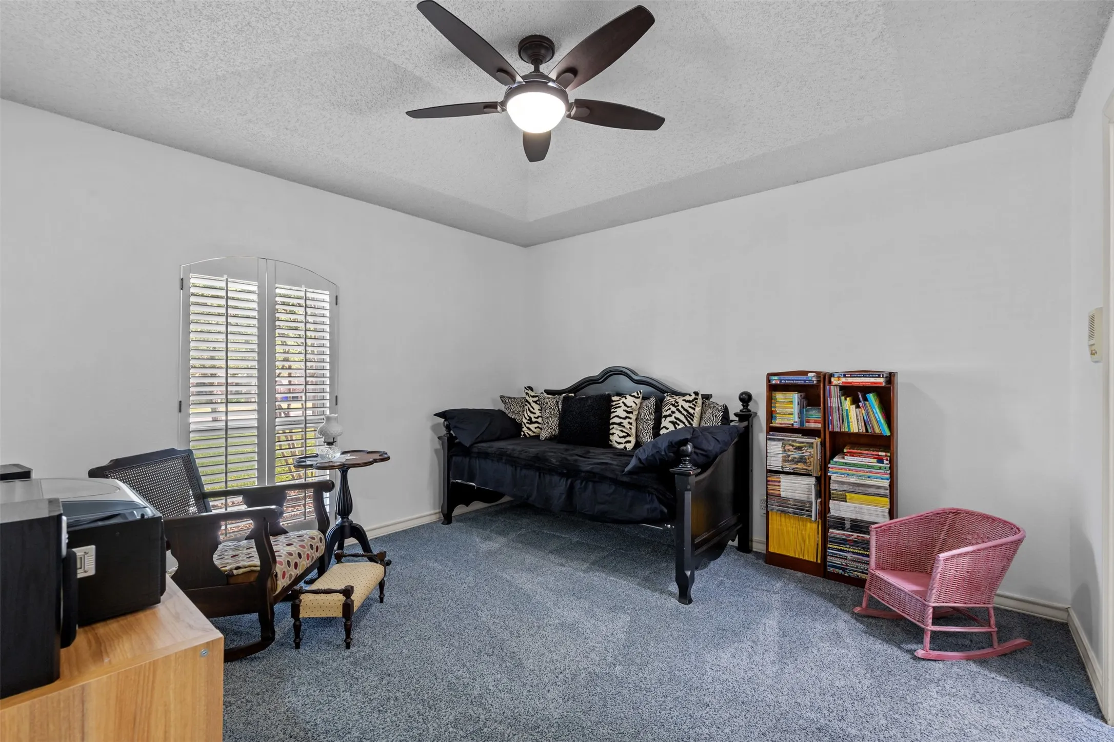 Carpeted room featuring a ceiling fan with integrated lighting, a tray ceiling detail, white walls, and a window with plantation shutters