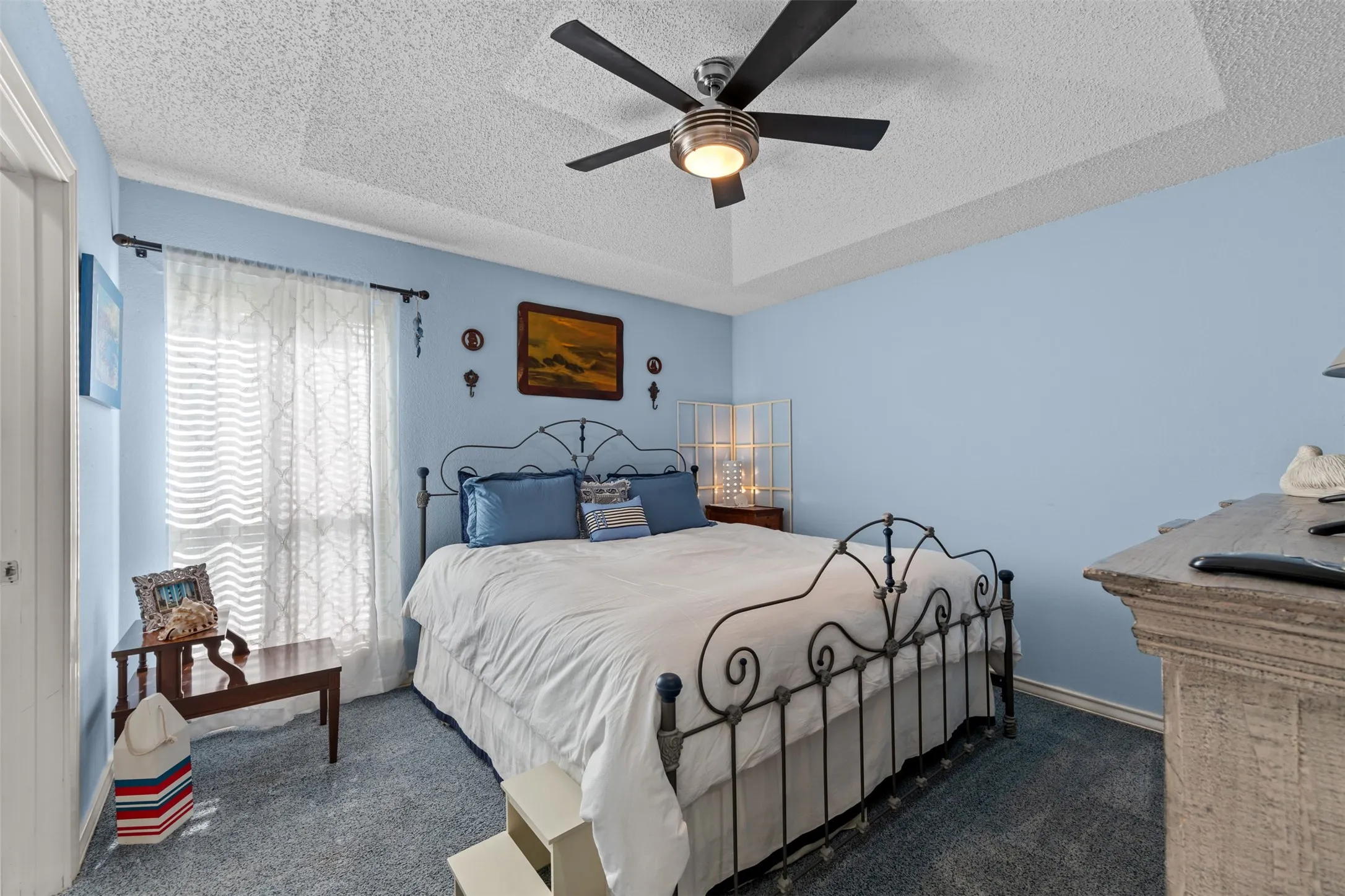 Recessed ceiling with a modern ceiling fan featuring integrated lighting, light blue wall paint, and a window with sheer curtains