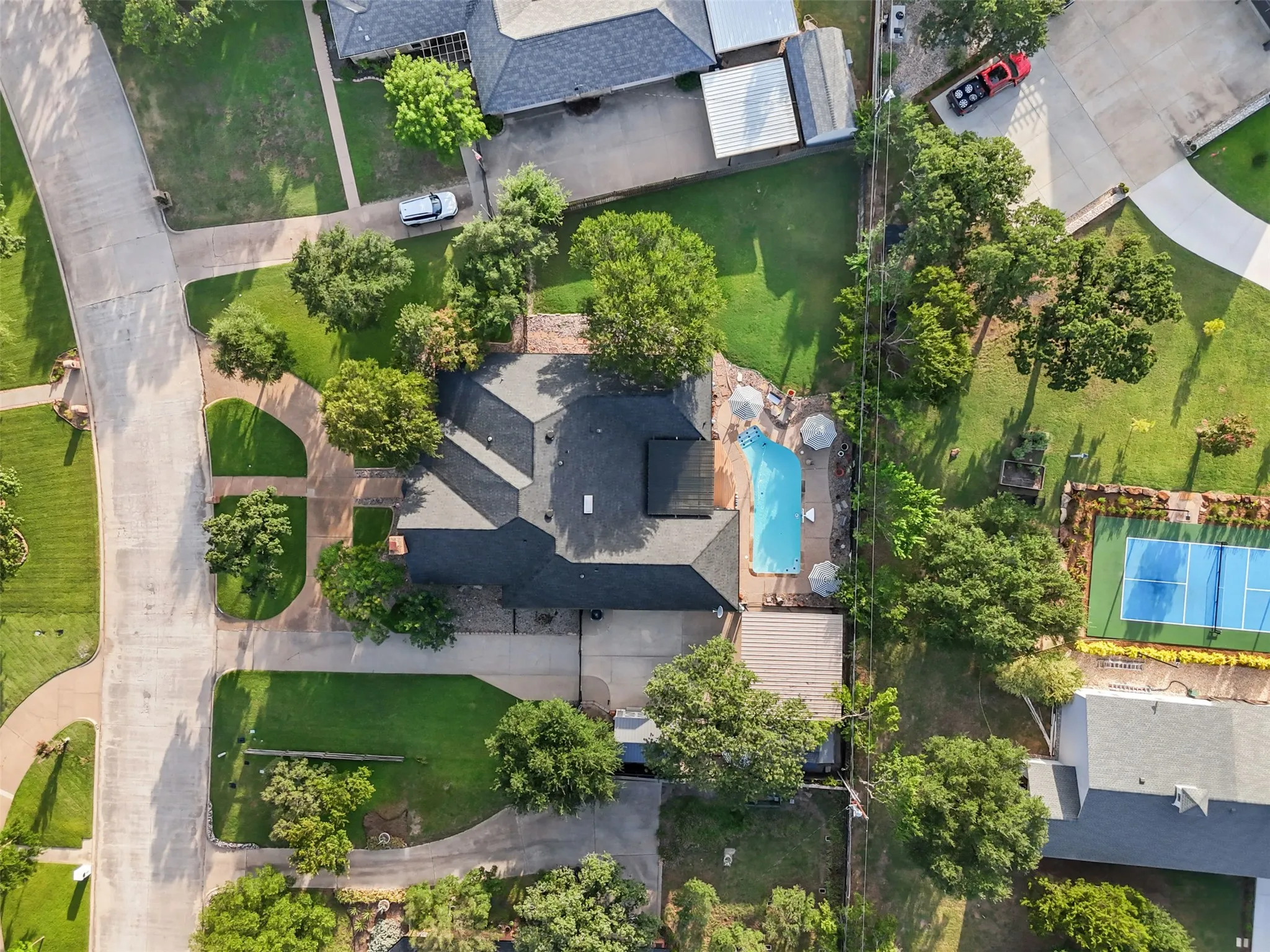 Expansive property featuring a dark-shingled roofline, a large outdoor swimming pool with surrounding patio space, and mature trees providing natural landscaping