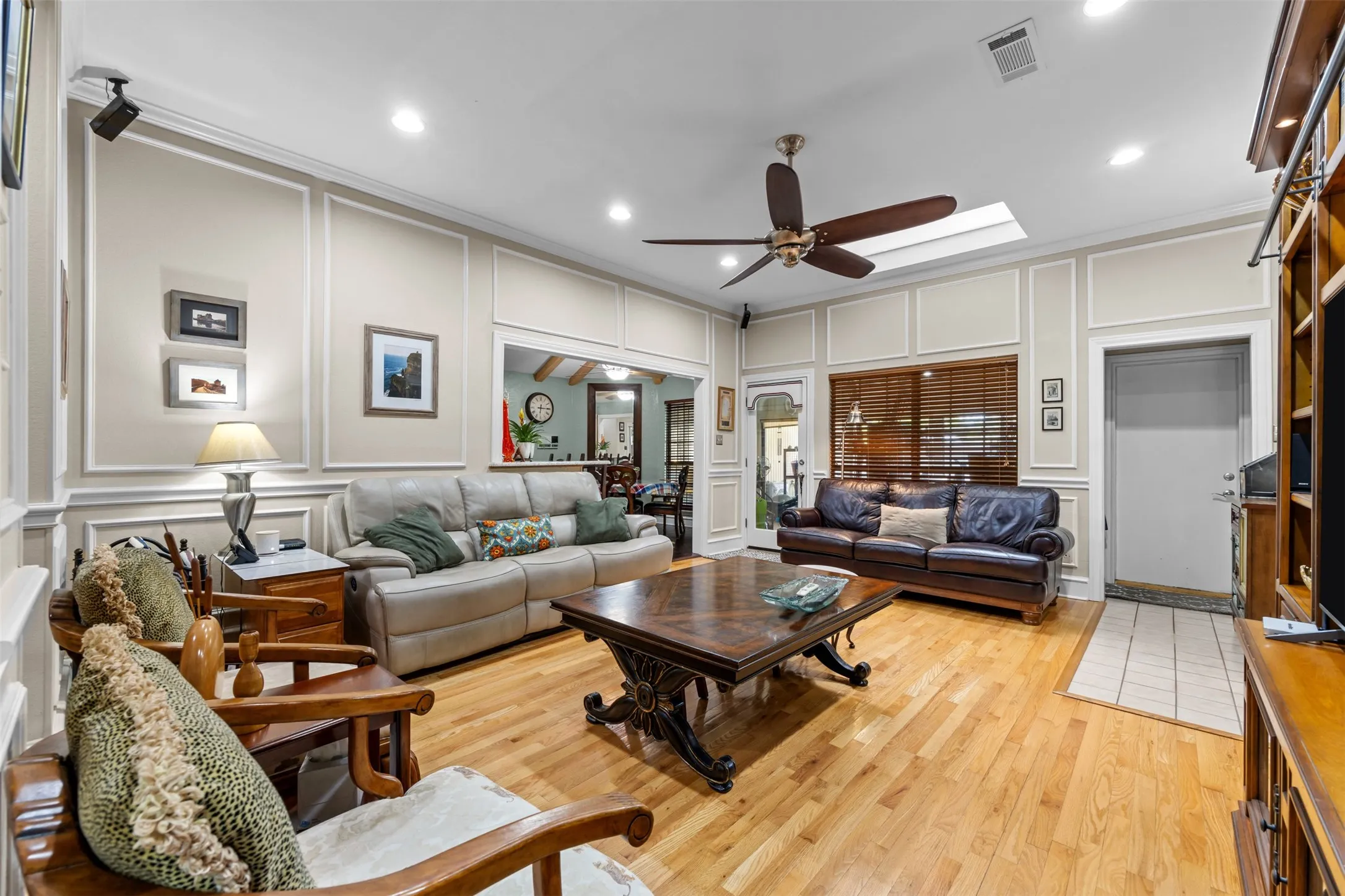 Living area featuring light wood-finish flooring, decorative wall molding, a ceiling fan, a skylight, and recessed lighting