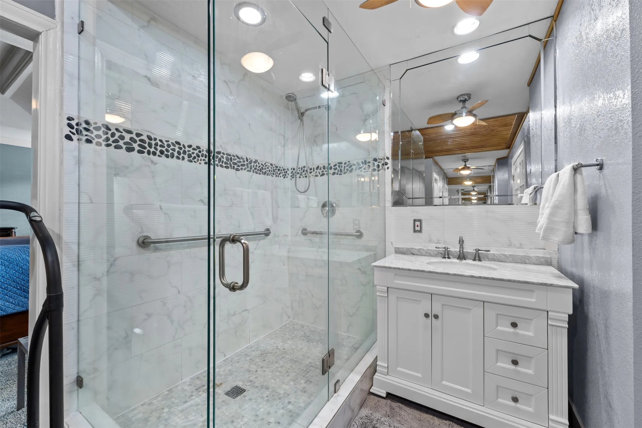 Glass-enclosed shower with a pebble tile accent band and mosaic tile floor
