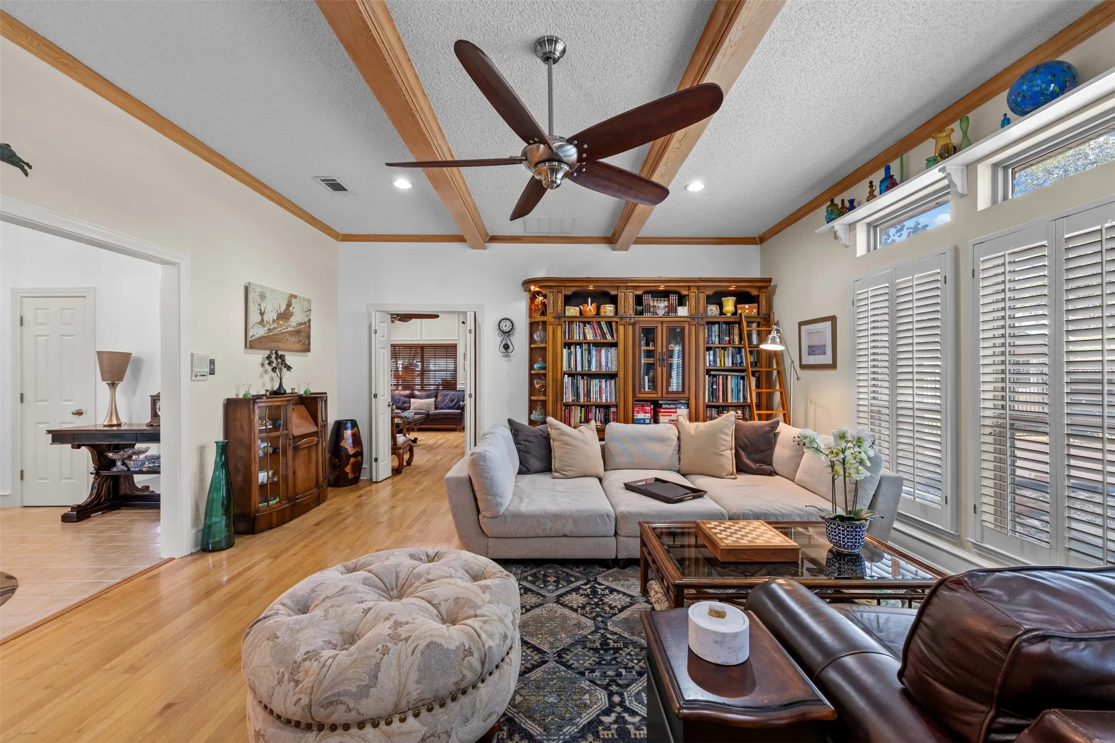 Spacious living area featuring wood-finish flooring, exposed ceiling beams, and a built-in bookcase