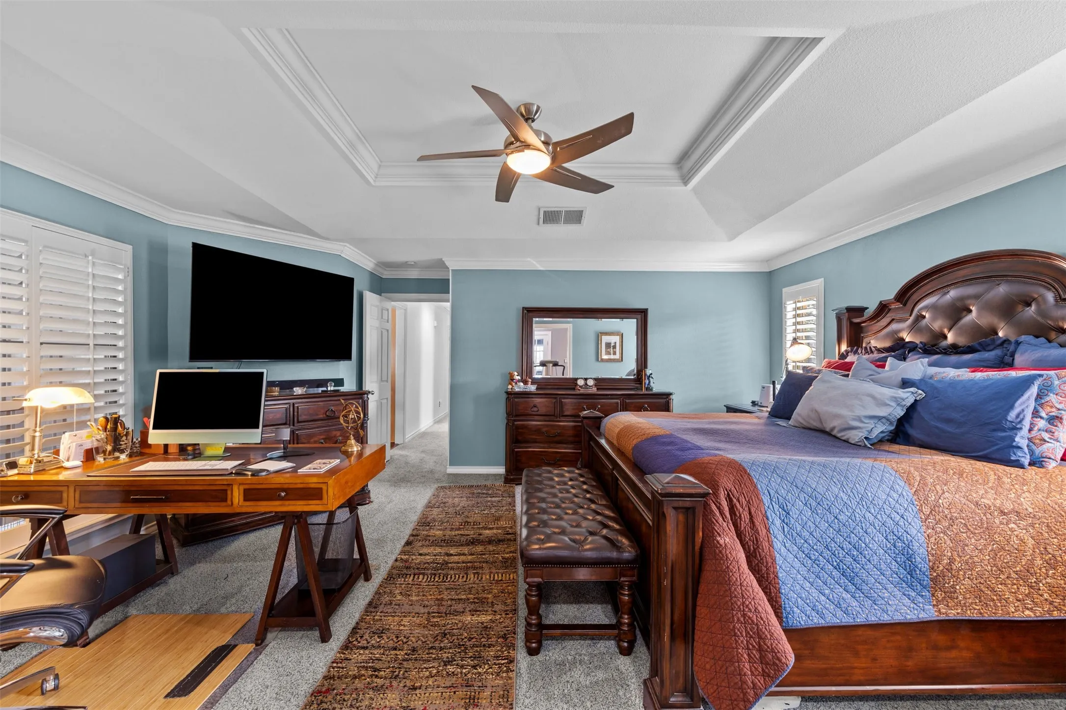 Spacious room featuring a tray ceiling with crown molding, ceiling fan, and plantation shutters