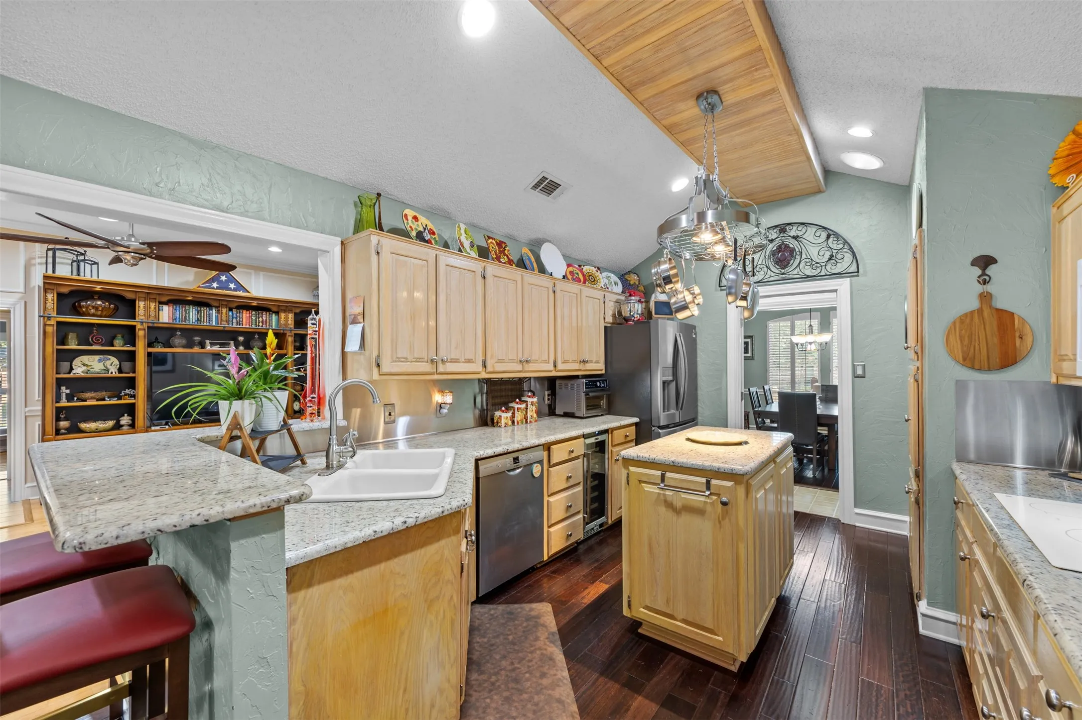 Kitchen featuring light wood cabinetry, granite countertops, a central island, dark wood-finish flooring, and a pot rack light fixture
