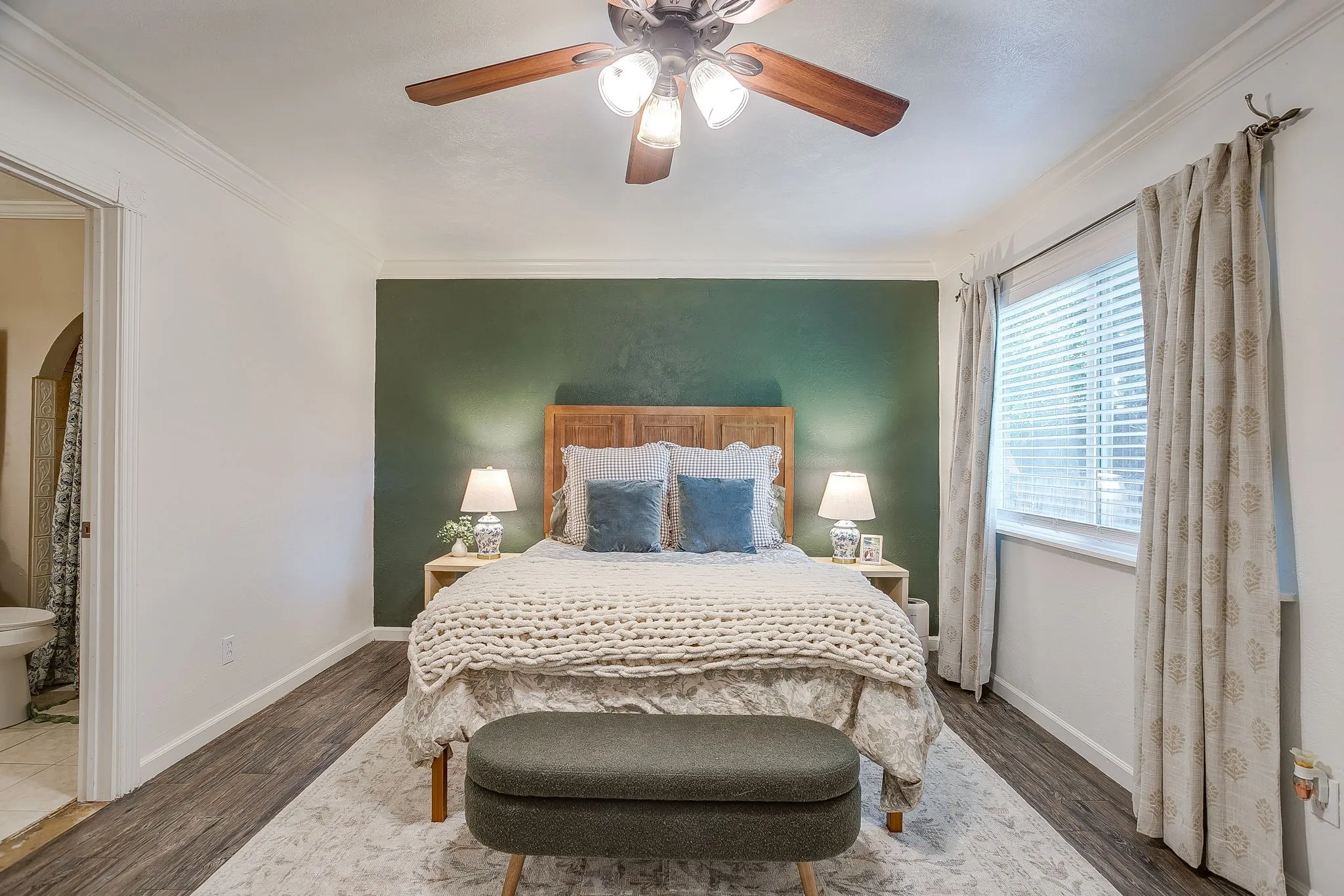 Calm and inviting primary suite with ensuite bath, accent wall, ceiling fan, and laminate flooring.