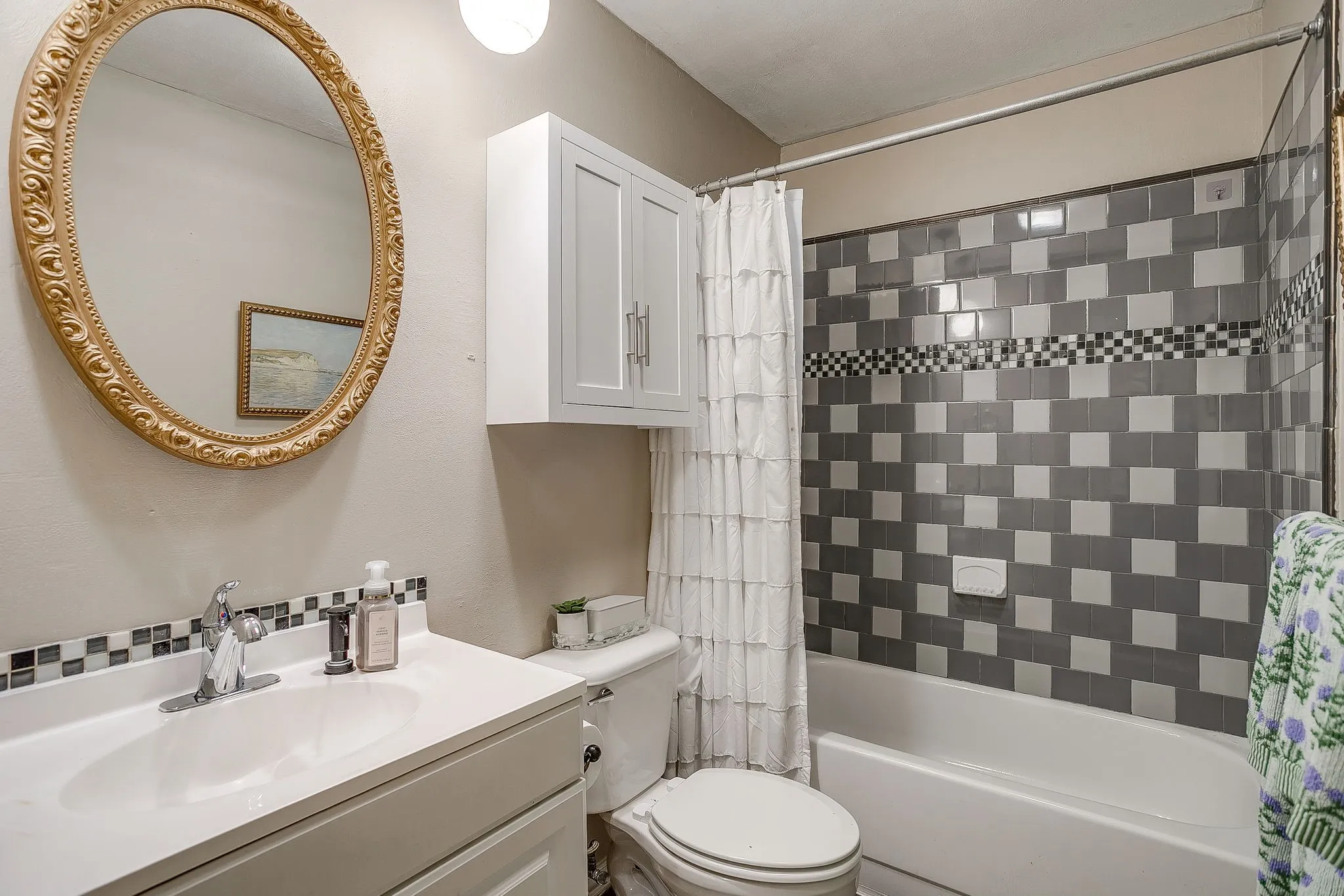 Secondary bathroom with tiled shower and tub combination, mounted cabinet, and custom mirror and tiled backsplash over vanity.