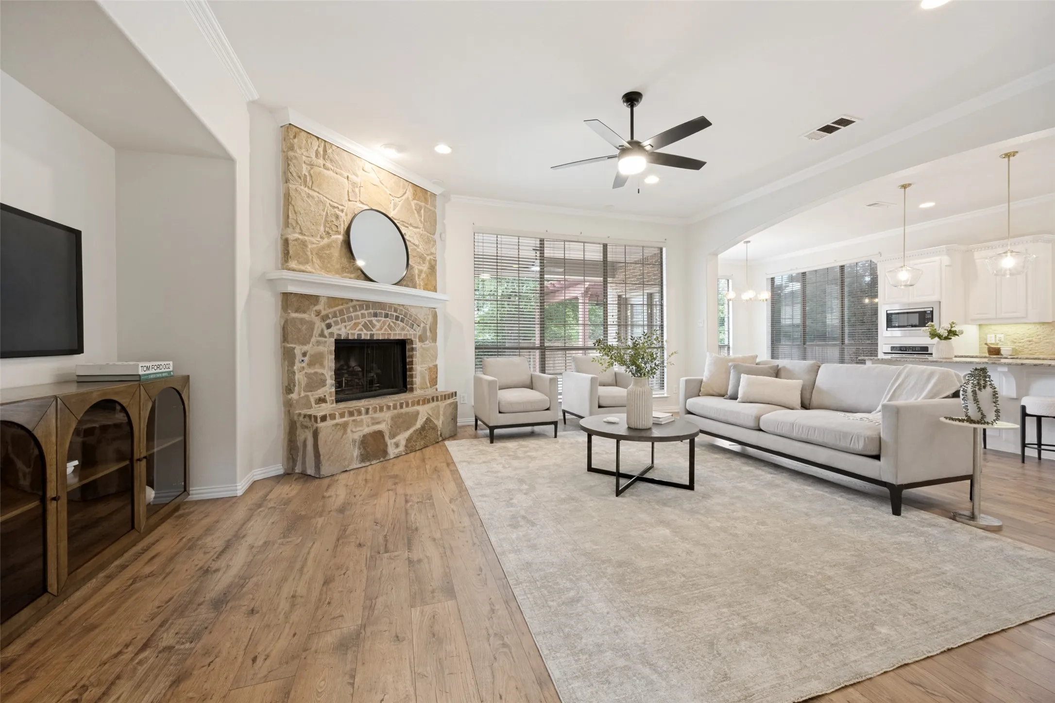 Spacious living area featuring a stone-clad fireplace with an arched firebox, wood-finish flooring, a contemporary ceiling fan, recessed lighting, and large windows looking out to the pool