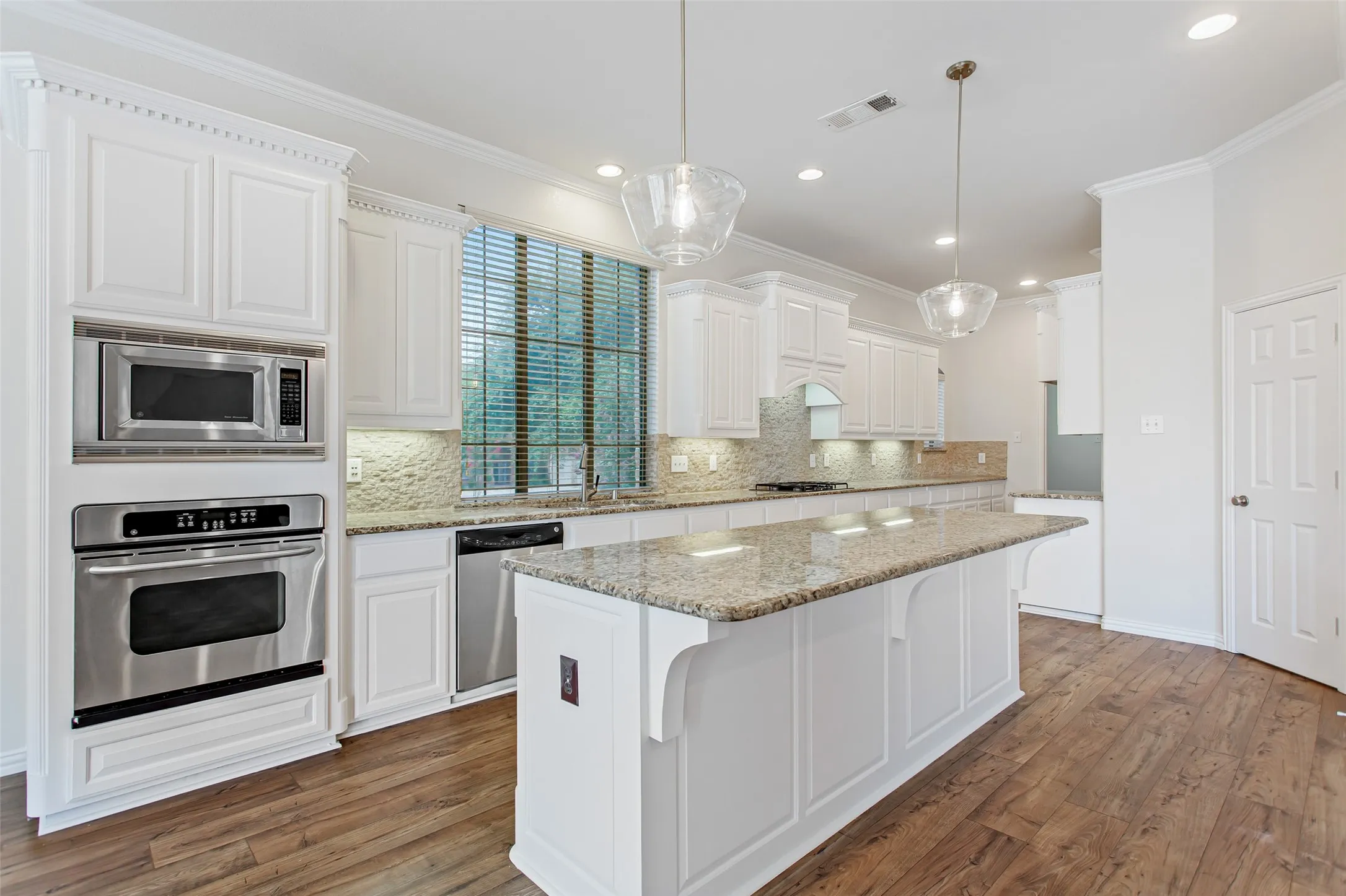 Bright and open kitchen featuring a central island with granite countertops, abundant white cabinetry, stainless steel appliances, and wood-finish flooring